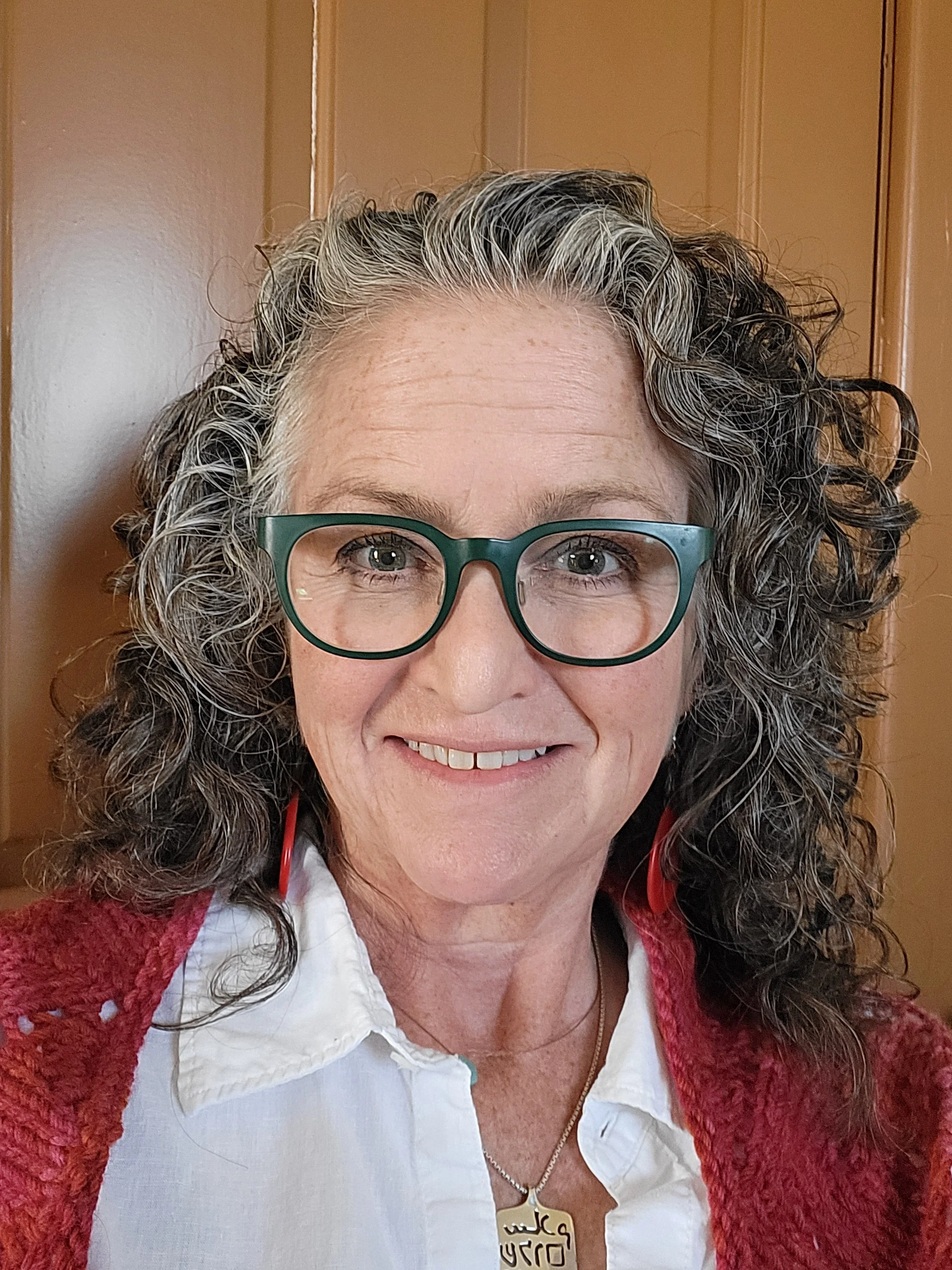 A woman with shoulder-length hair smiling, wearing a white top with a red sweater.