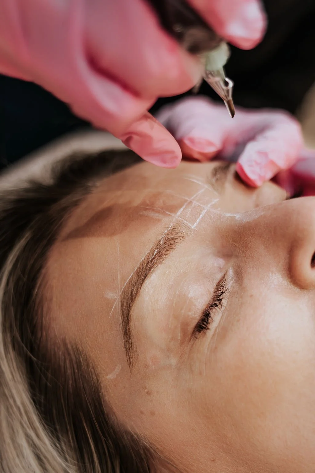 A woman receiving an eyebrow tattoo treatment from a technician in a clinic setting.