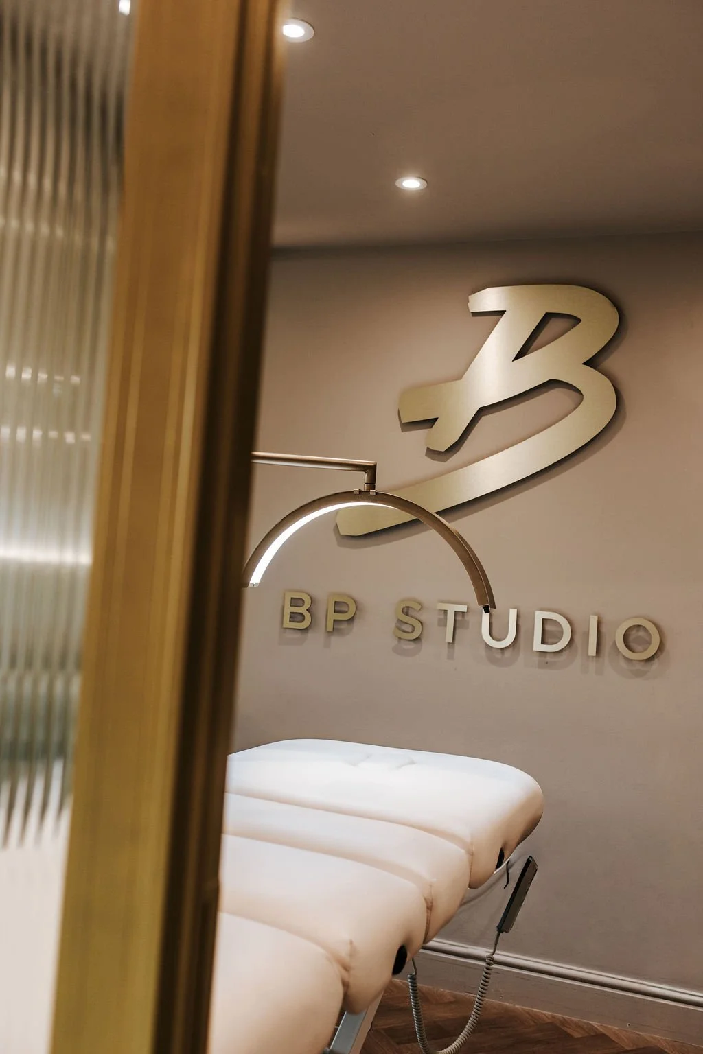 Interior of a beauty clinic with a beige massage bed, a wall sign reading 'BP STUDIO' with a large B above, and subdued lighting.