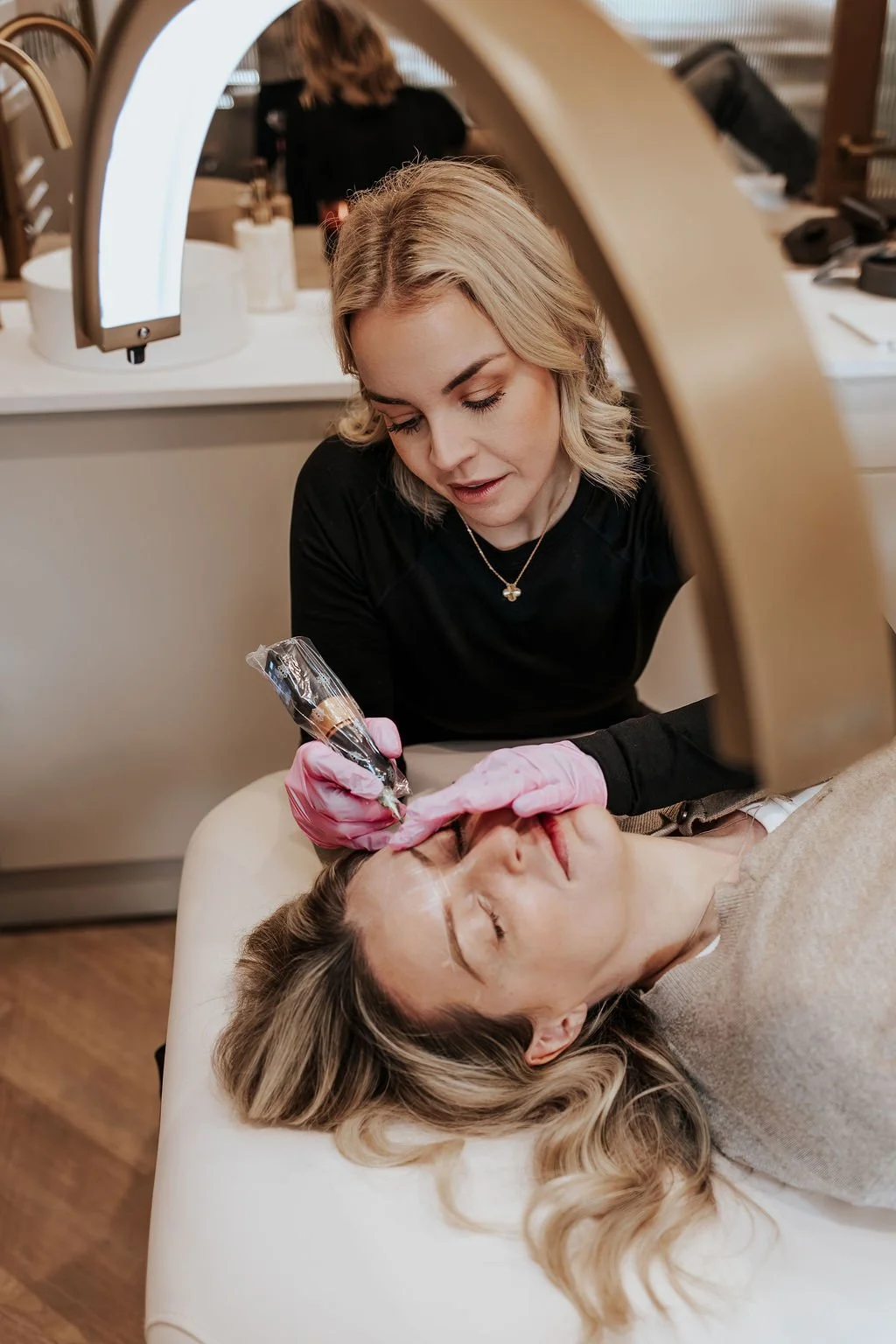 A woman receiving an eyebrow tattoo treatment from a technician in a clinic setting.
