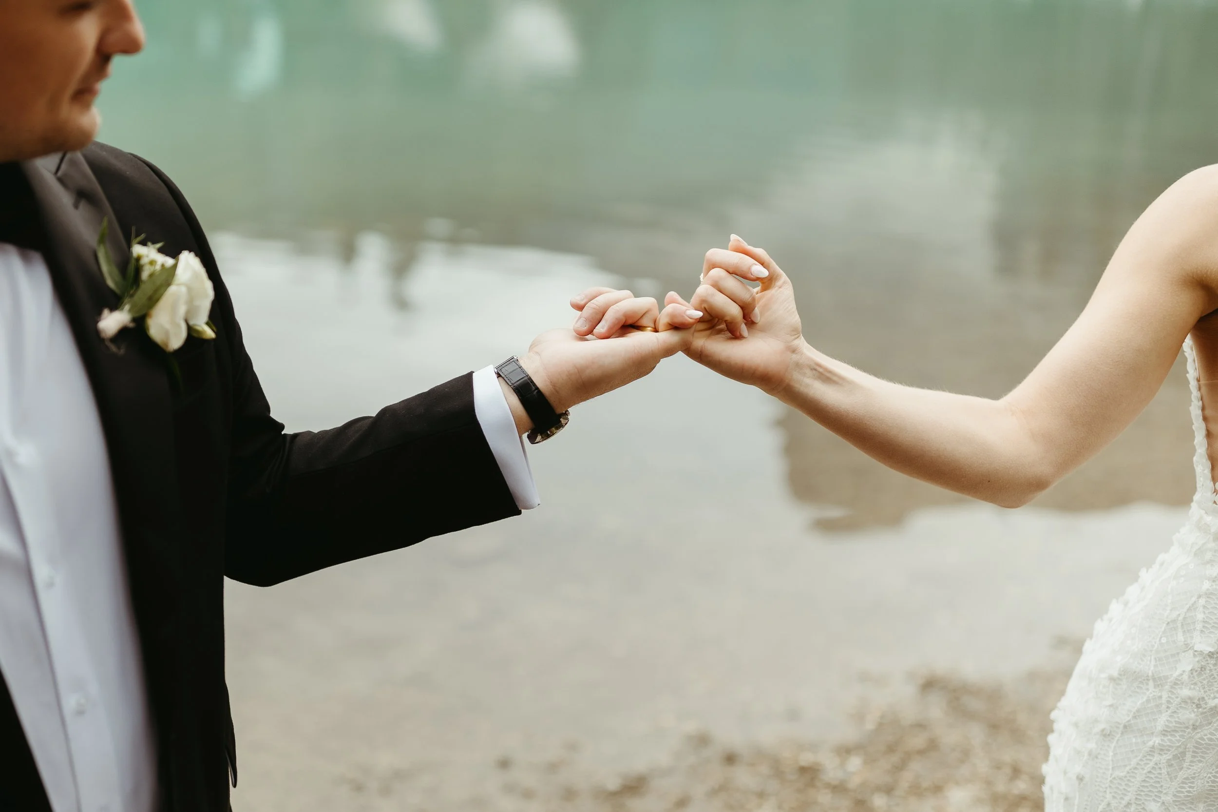 Bride and groom pinky promise with Emerald Lake in the background