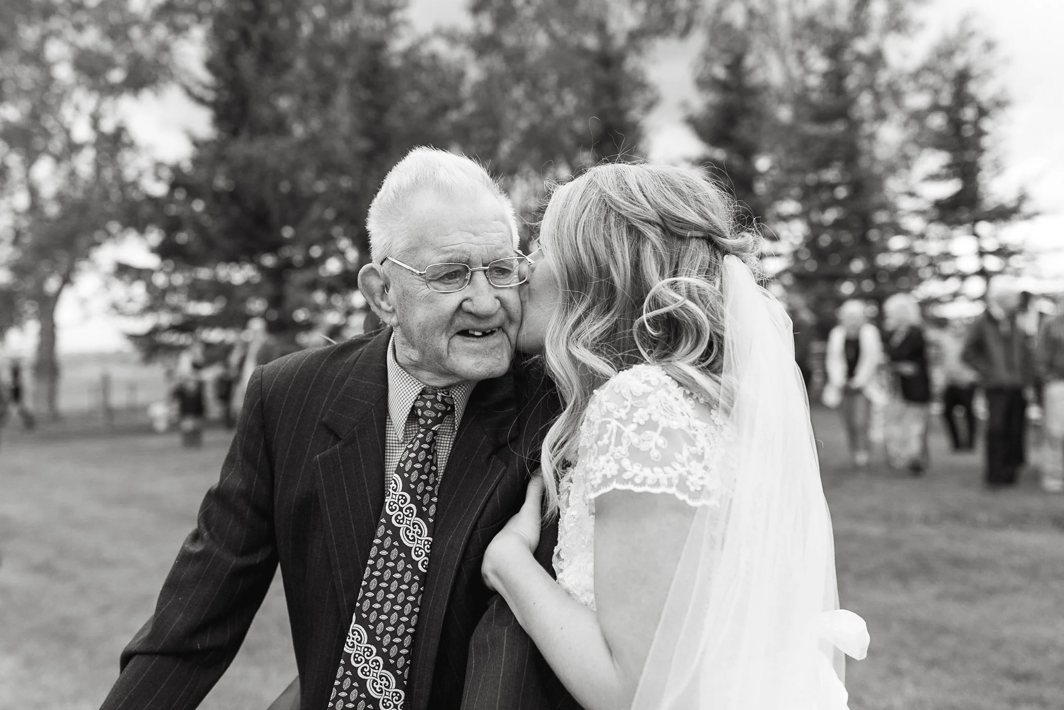 Documentary black and white photo of bride kissing her grandpa at her wedding at The Gathered farm venue in Calgary, Alberta