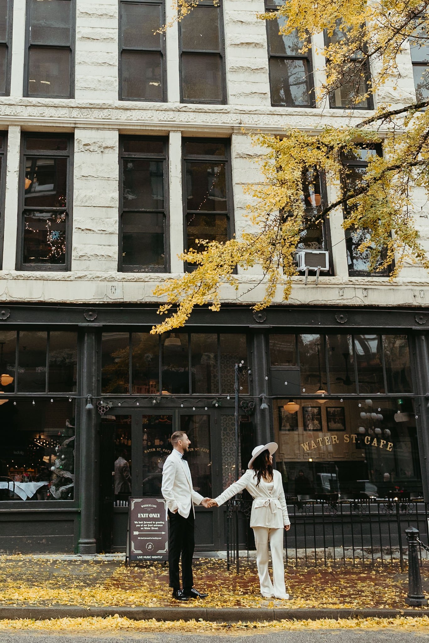 Couple holding hands in front of Water St. Cafe in Gastown with fall leaves on the ground.