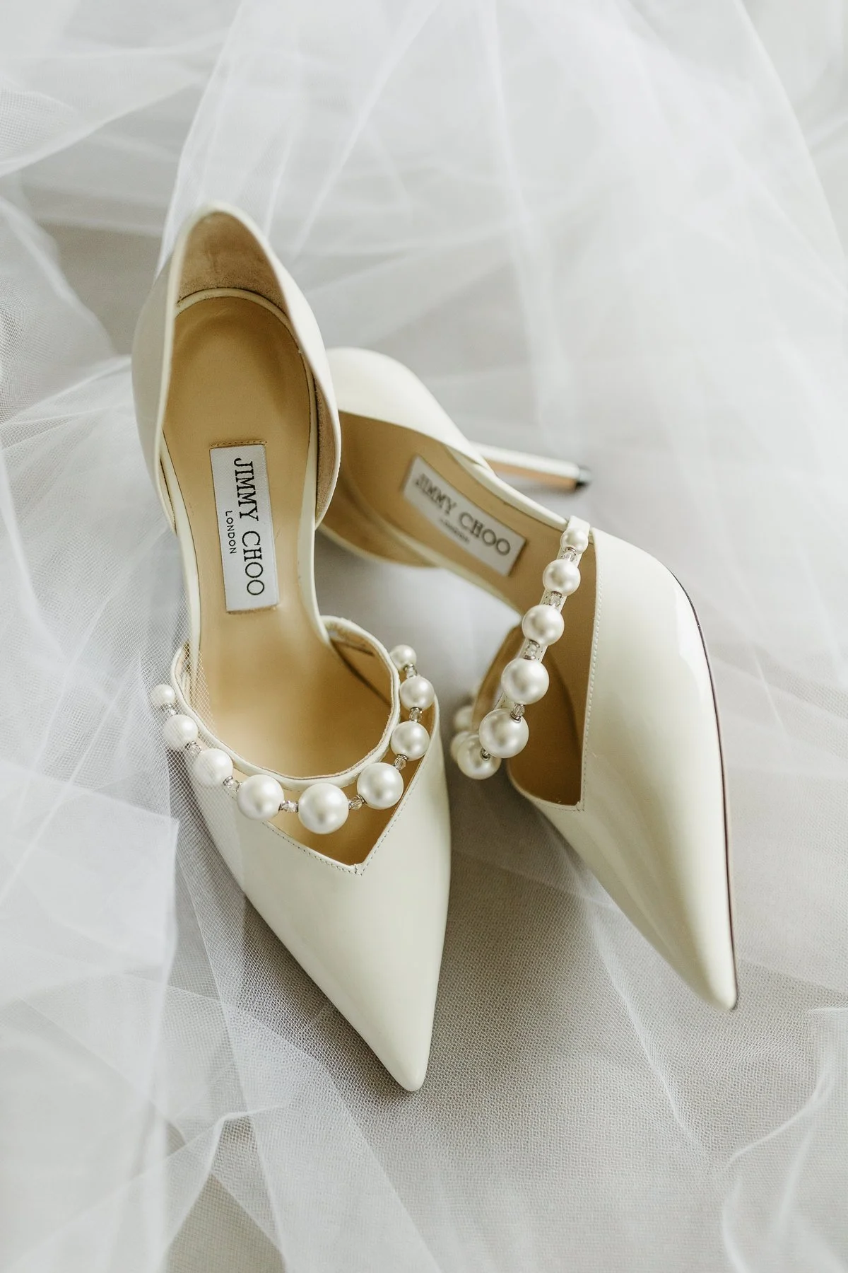 Elegant white high heels with pearl embellishments on sheer fabric.