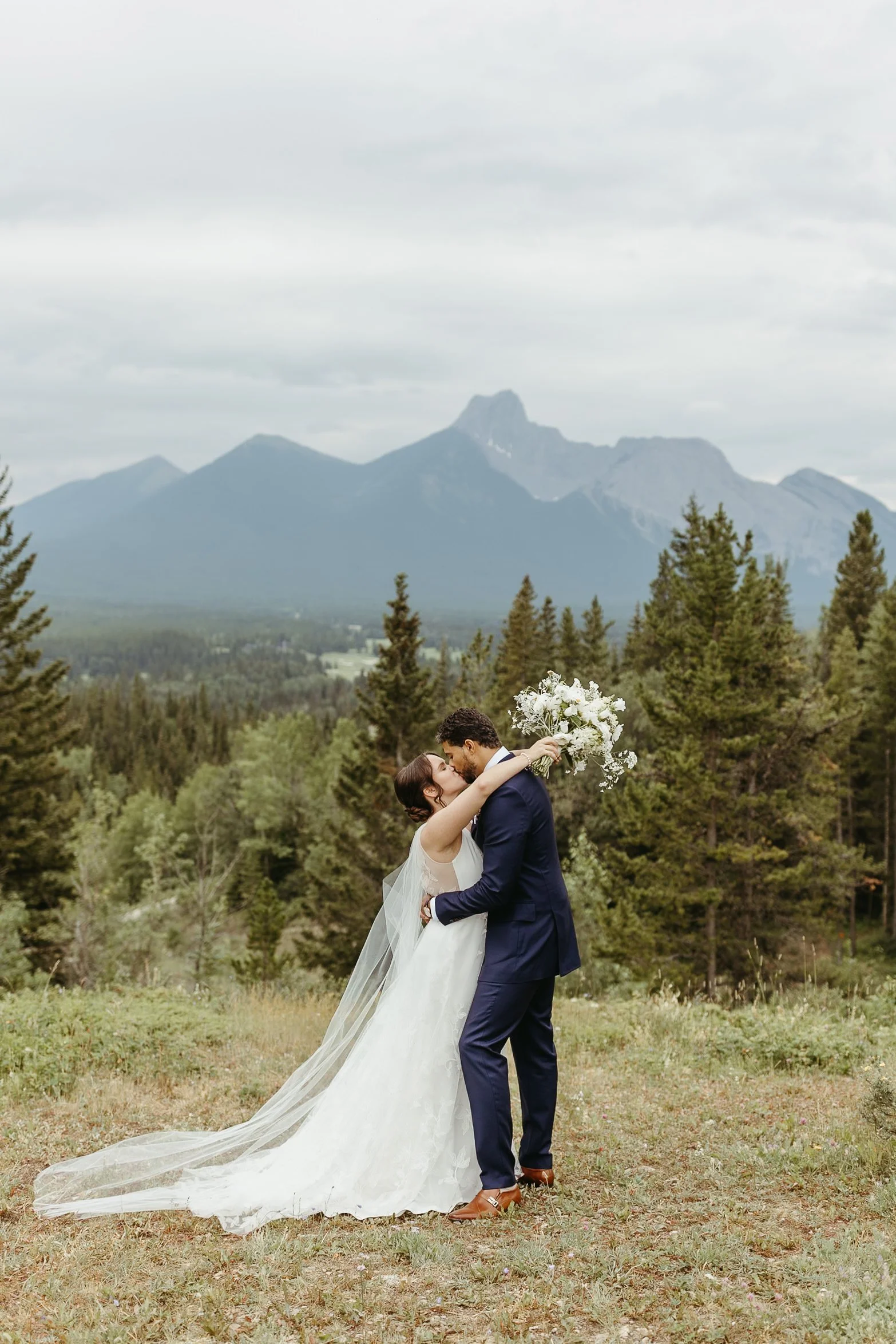 Bride and groom kiss with Rocky Mountains in the background at their intimate wedding in Kananaskis, Alberta