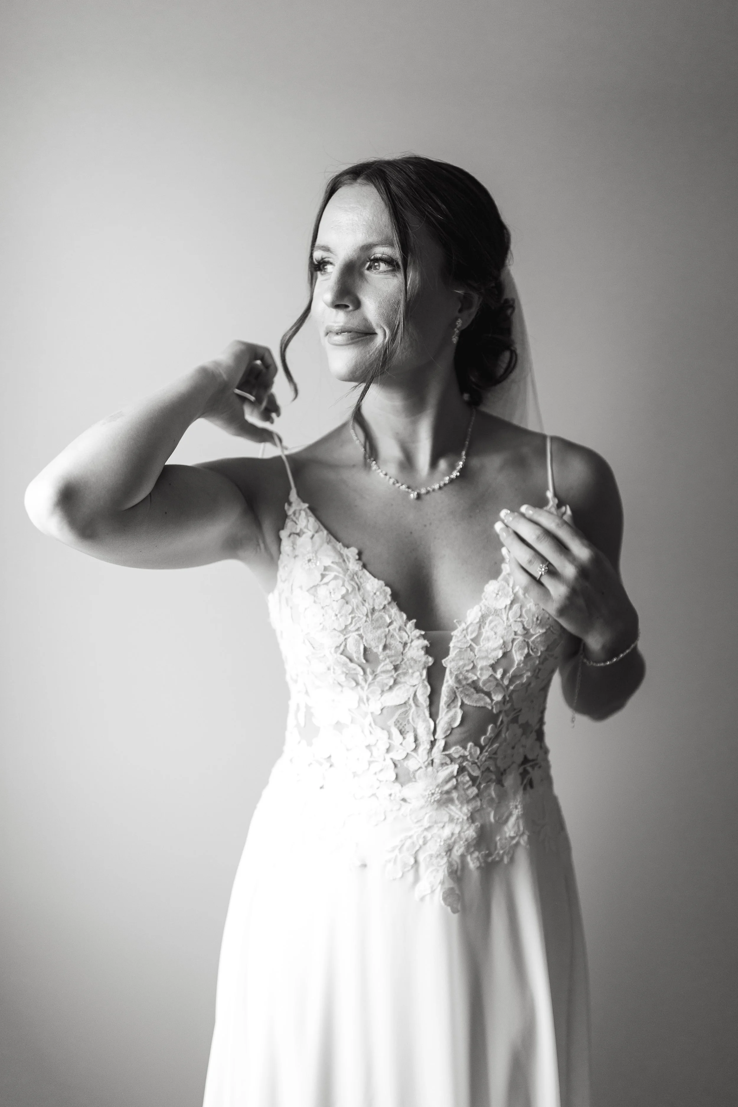 Black and white photo of bride in lace dress looking out the window on the morning of her wedding in Calgary