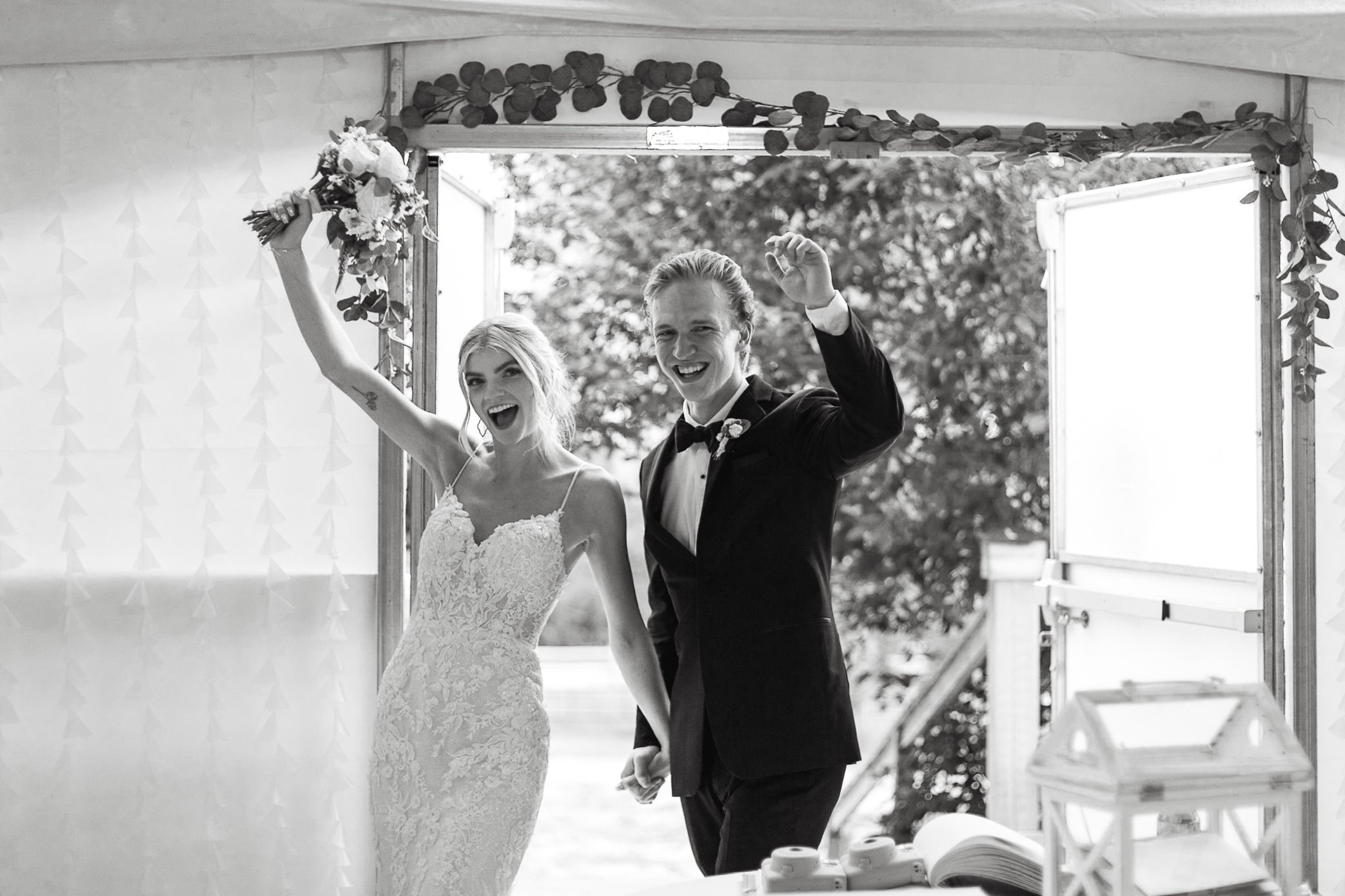 Black and white photo of bride and groom cheering as they walk into wedding reception at tented wedding venue outside Calgary, Alberta