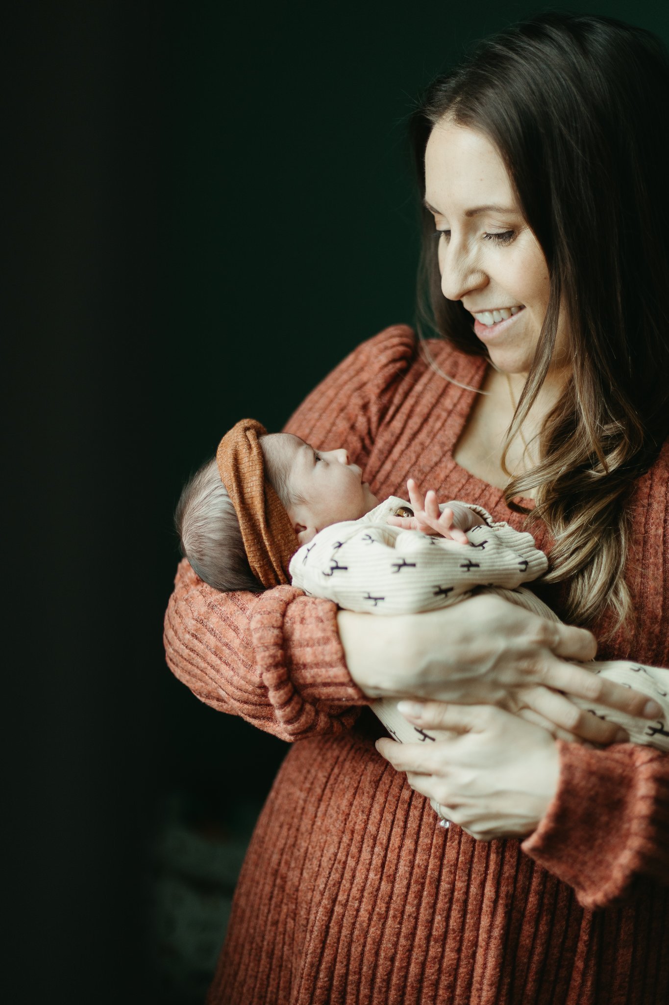 Candid photo of mother smiling at her newborn baby with an orange bow on her head 