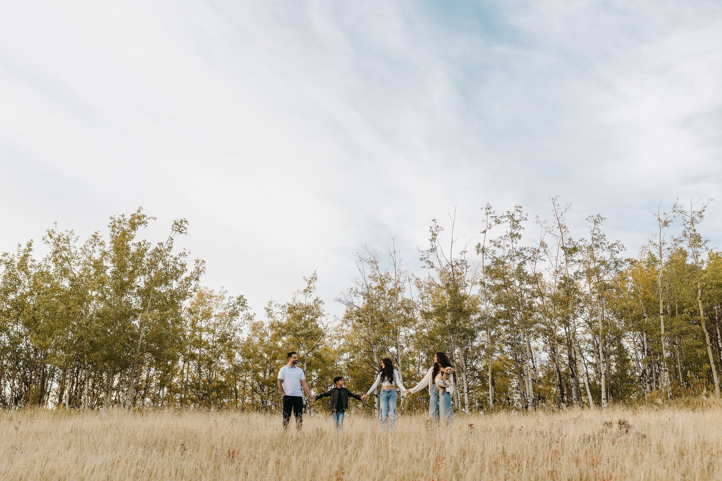 Family stands in the dry grass during candid fall family photo shoot in Calgary