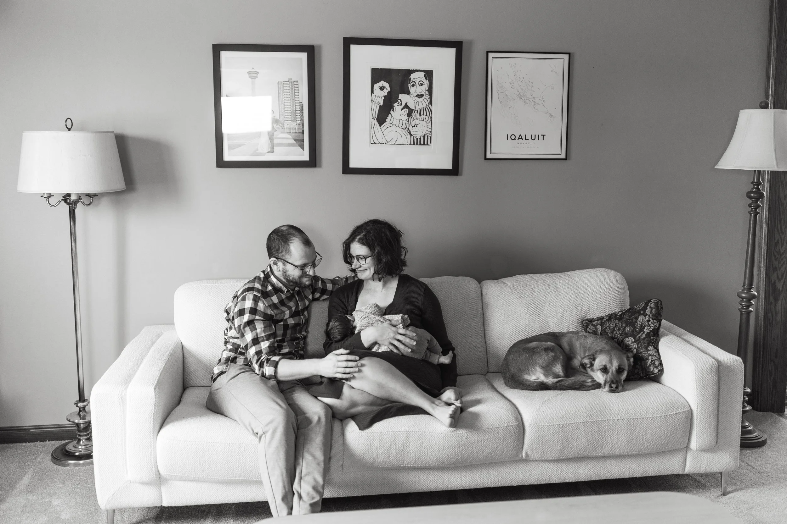 Candid black and white photo of couple at home on the couch with their newborn baby and dog 