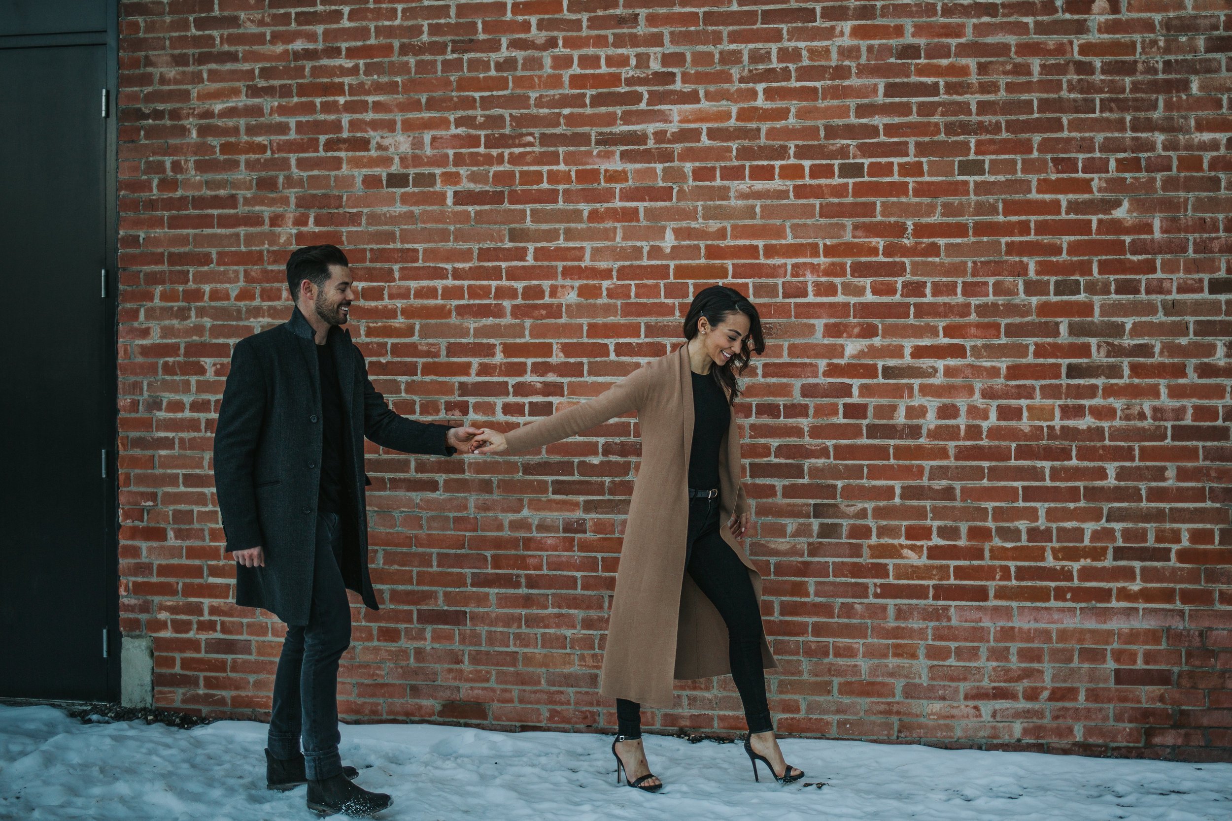 Couple waking along brick wall in downtown Calgary's East Village engagement session