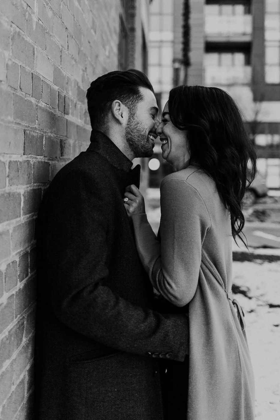 Black and white image of couple snuggling against a brick wall in downtown Calgary