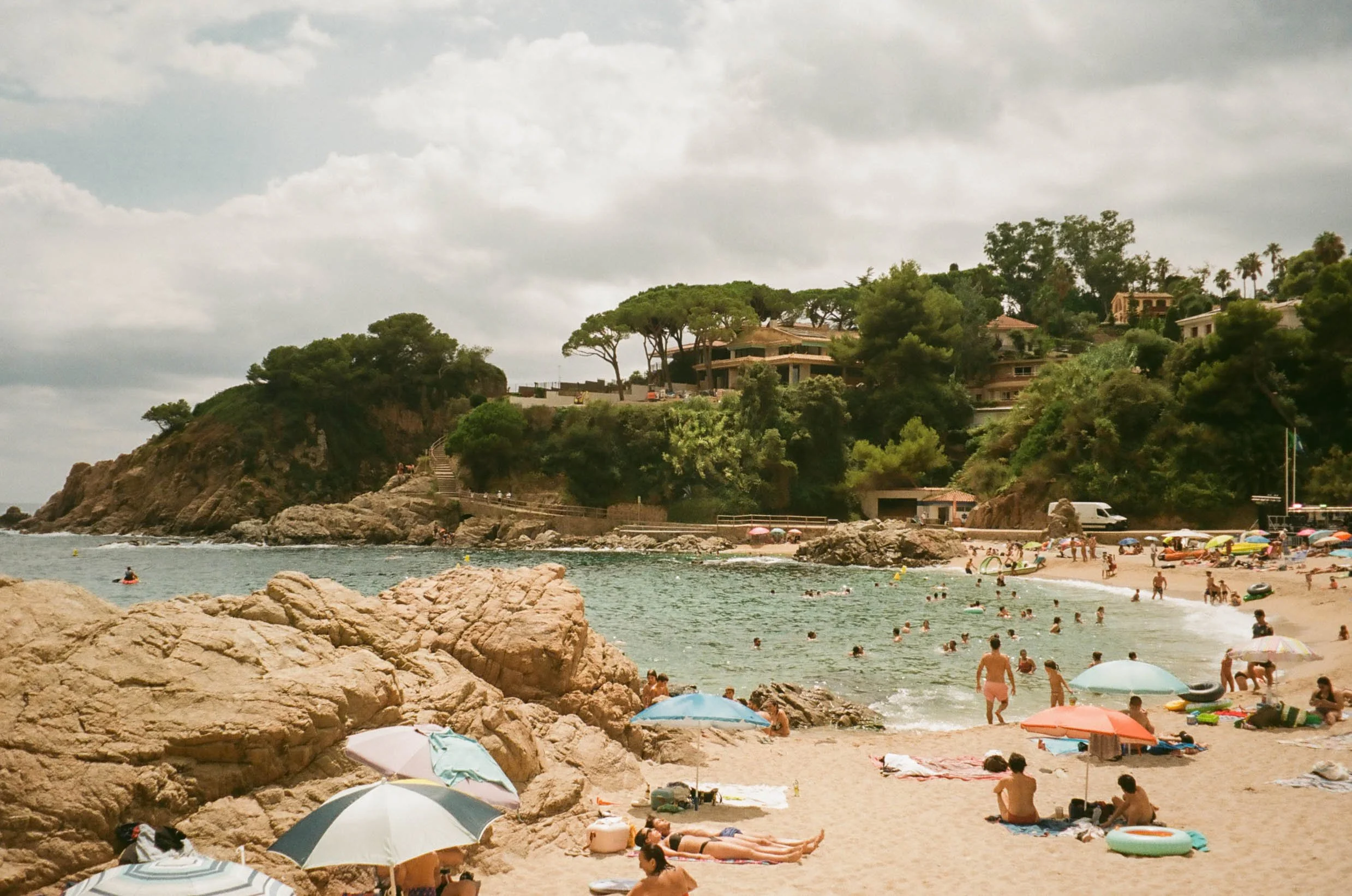 Film photo of beach in Costa Brava, Spain with rocky cliffs and sunbathers