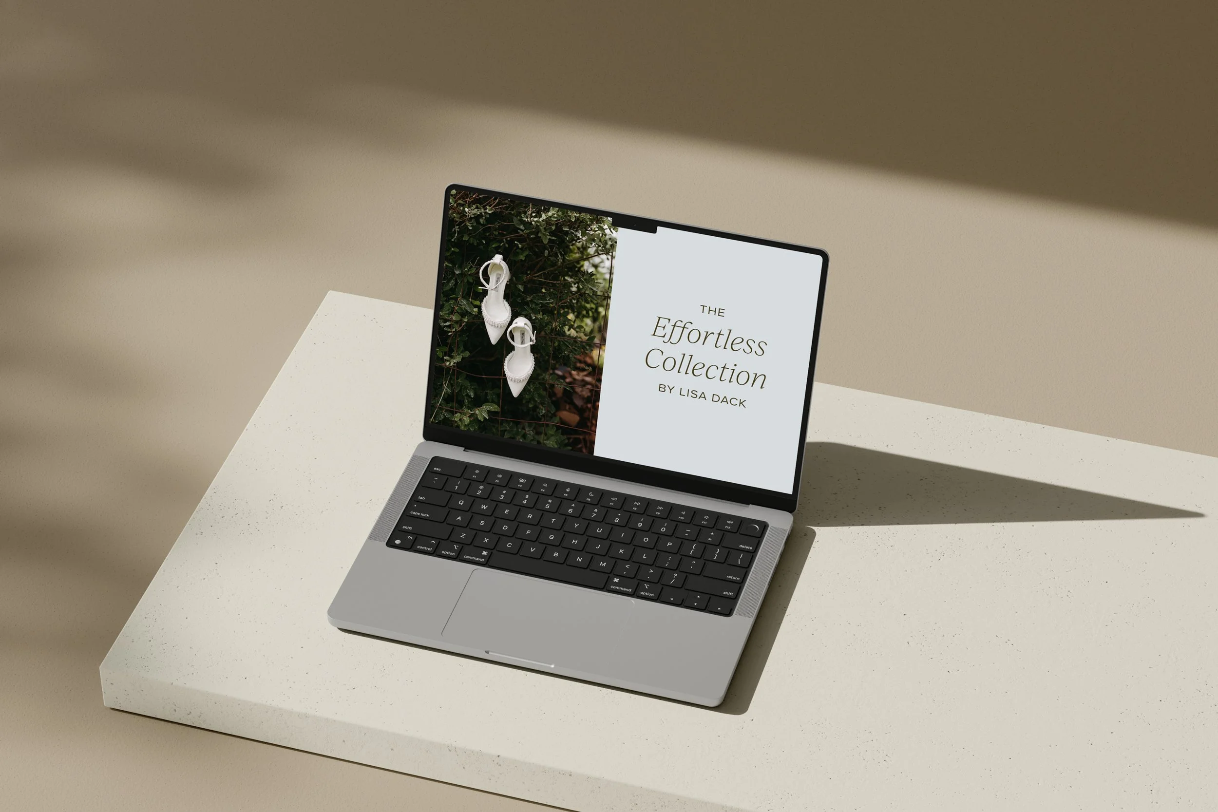 A laptop on a white surface displaying a fashion collection presentation titled 'The Effortless Collection by Lisa Dack', with images of white shoes hanging on a green leafy background.