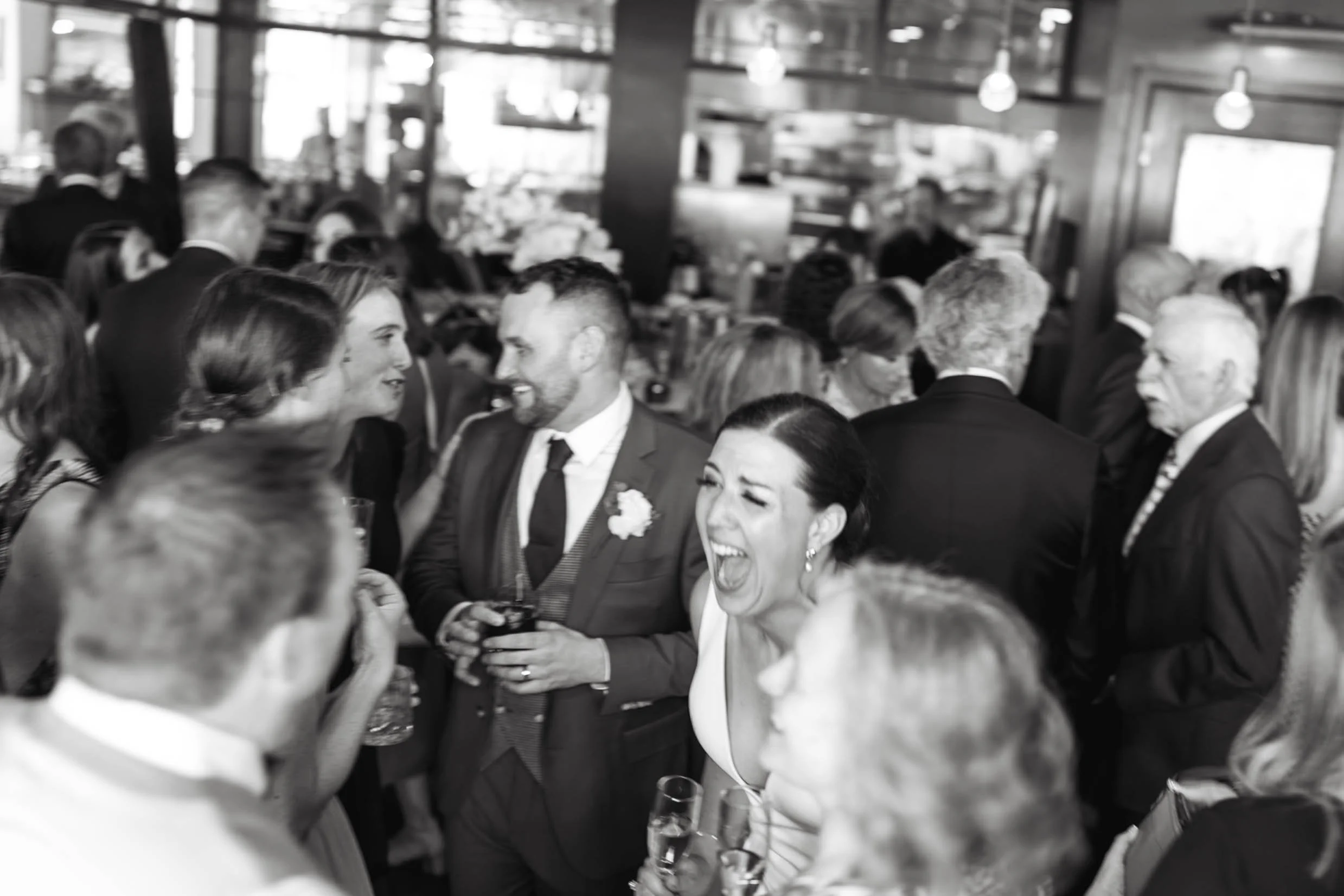 Candid black and white photo of bride and groom laughing with their guests during cocktail hour on their wedding day at The Nash in Calgary 