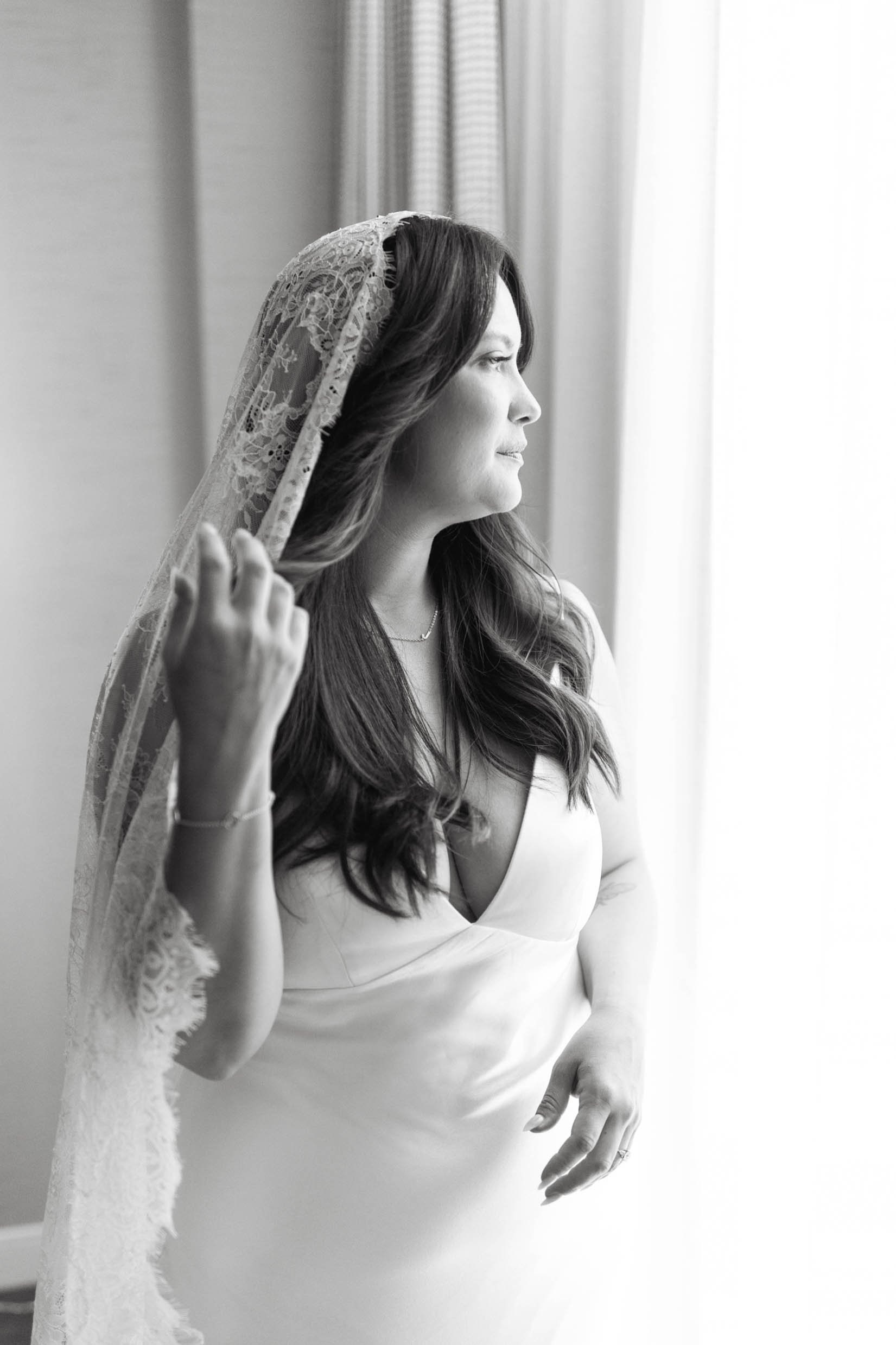 Black and white portrait of bride in lace veil looking out her hotel window on her wedding day at the Dorian Hotel in Calgary 