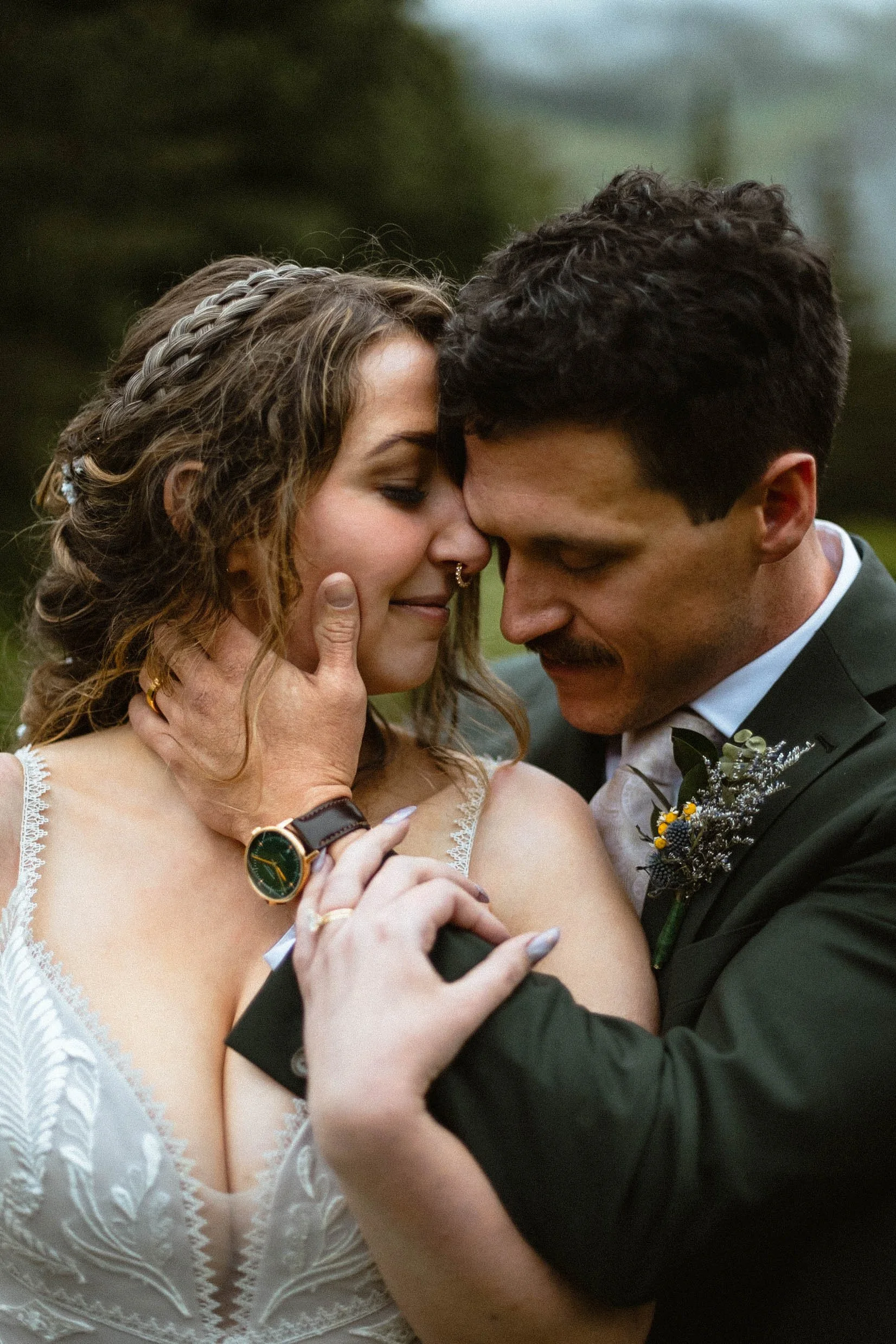 Bride with braided hairstyle embraces her groom in dark green suit on their rainy wedding day at Island Lake Lodge in Fernie, BC