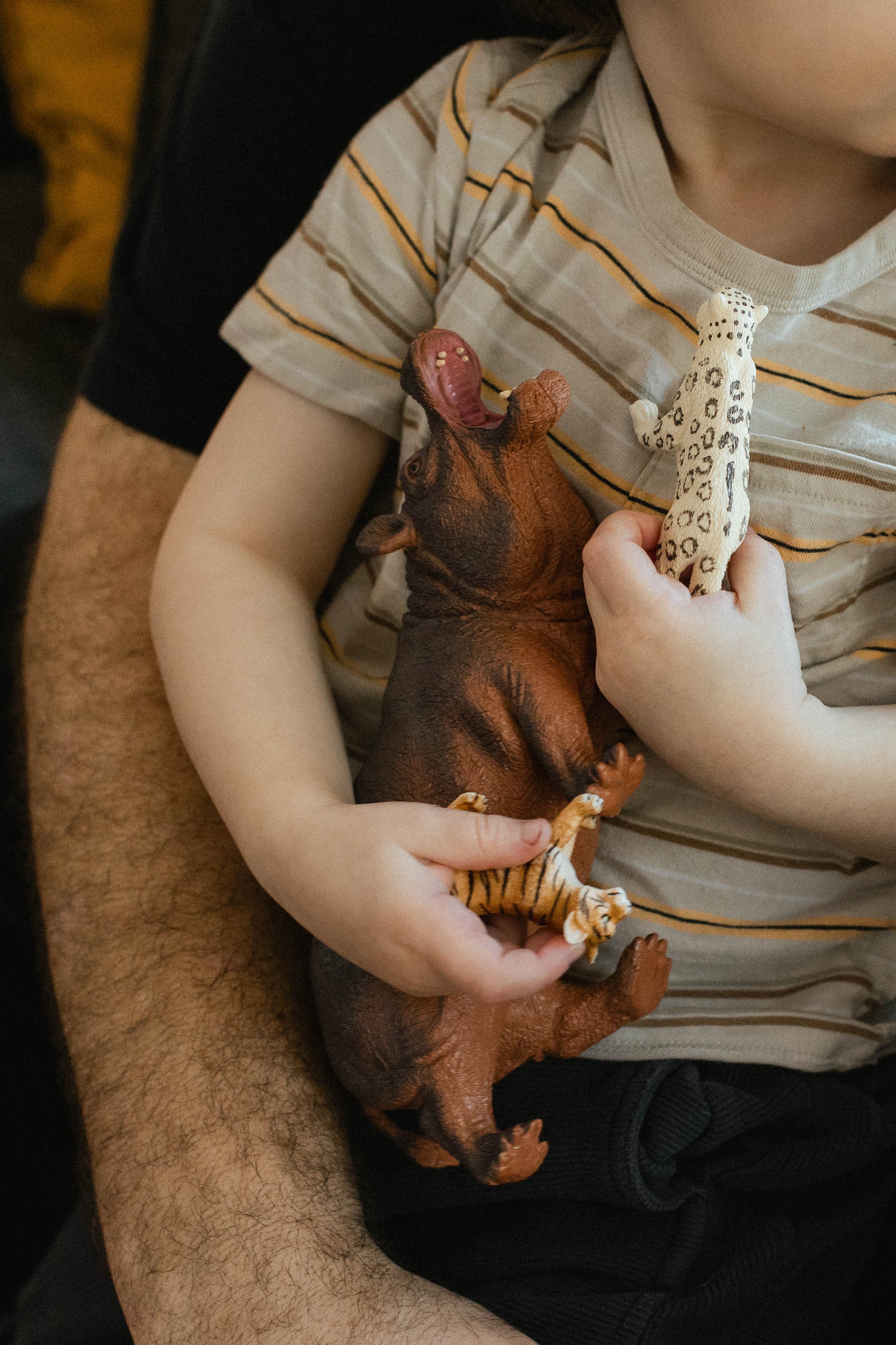 A child in a striped t-shirt holds an armful of plastic wild animal toys in his small hands