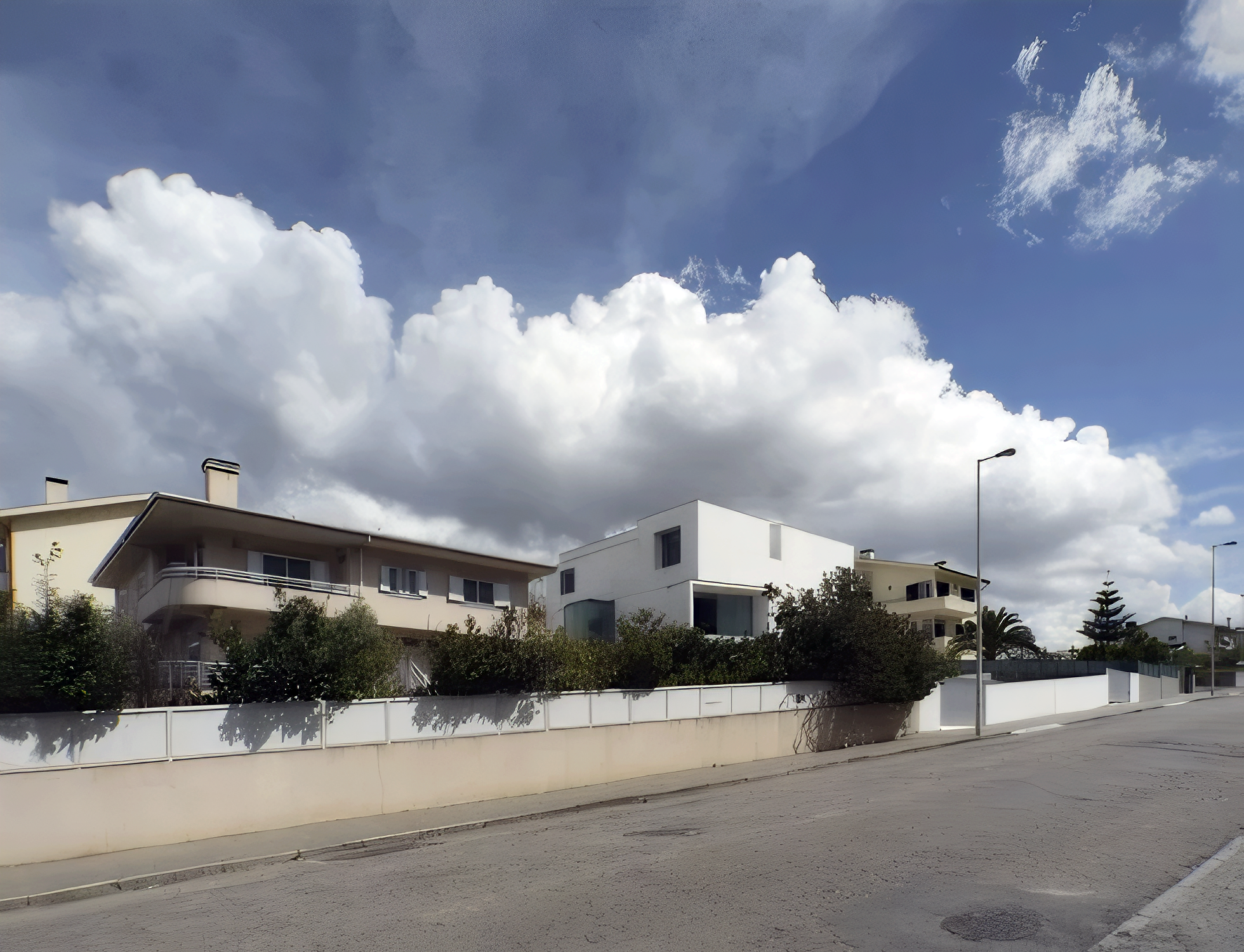 Casas modernas de duas andares com jardins em uma rua tranquila, sob céu parcialmente nublado.