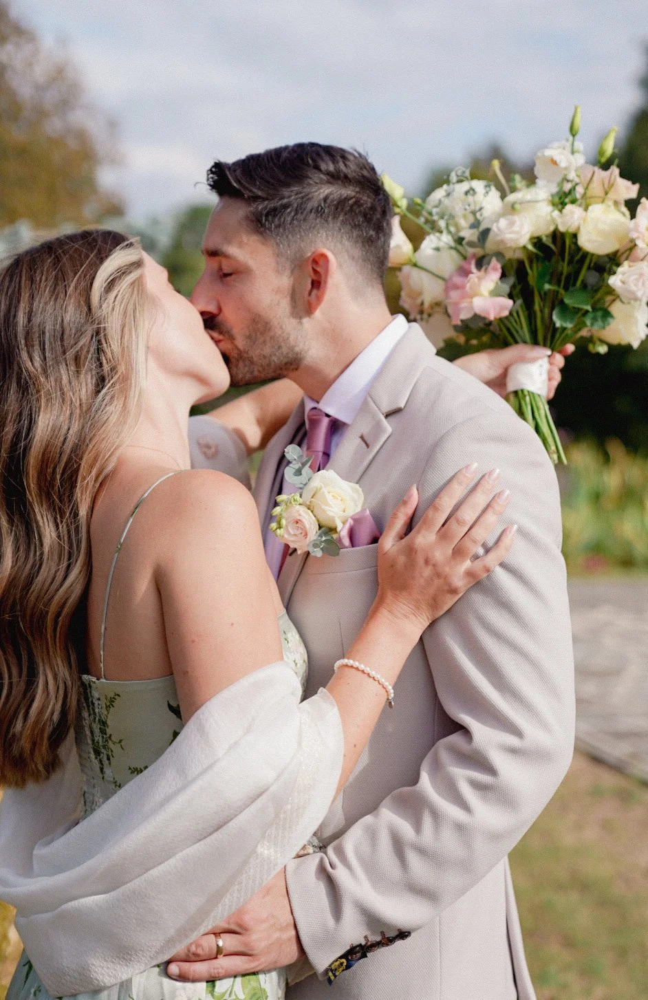 A couple sharing a kiss at their wedding, with the woman holding a bouquet of flowers behind them.