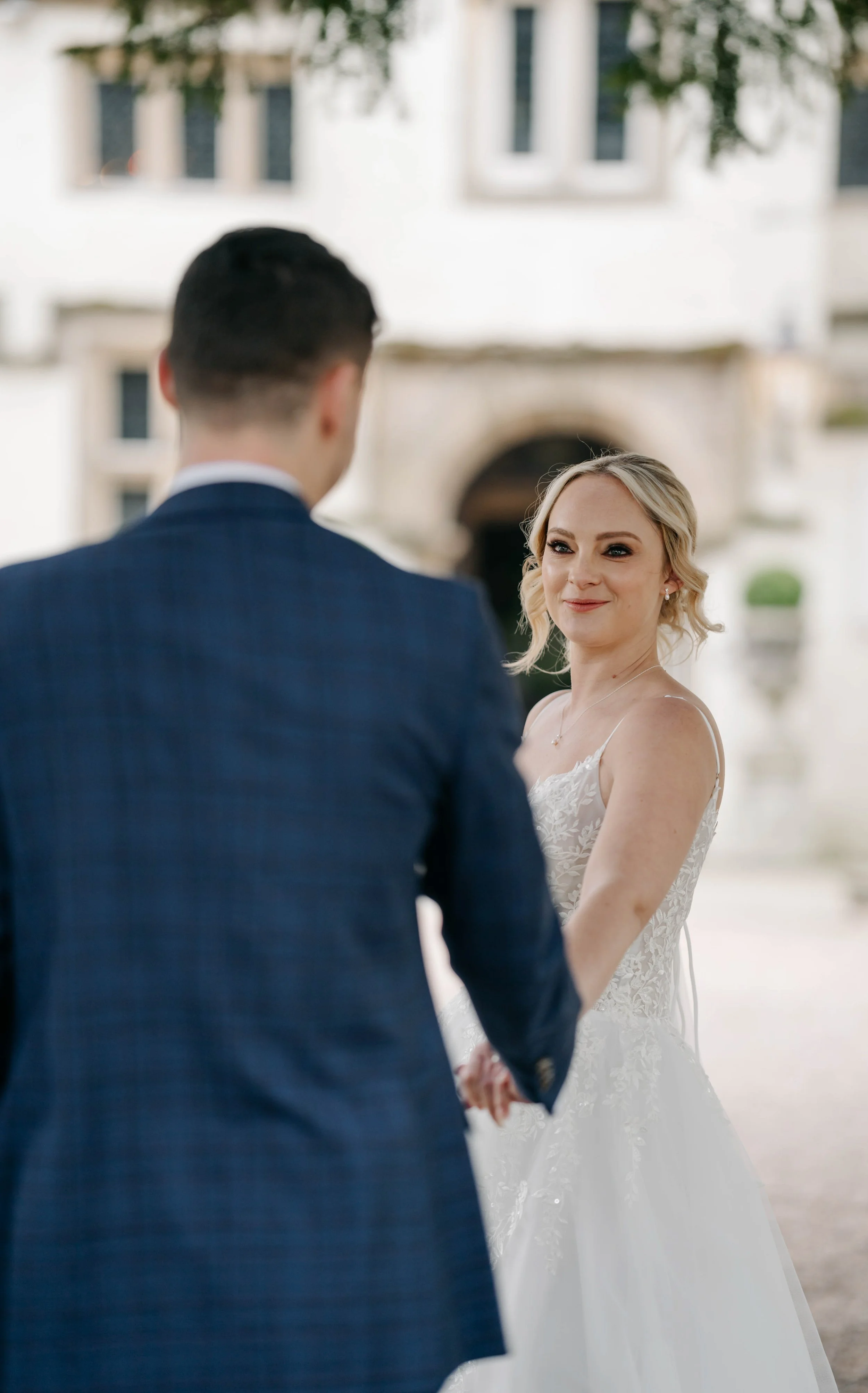 A bride and groom holding hands during their wedding ceremony outdoors, with the bride smiling and looking at the groom.