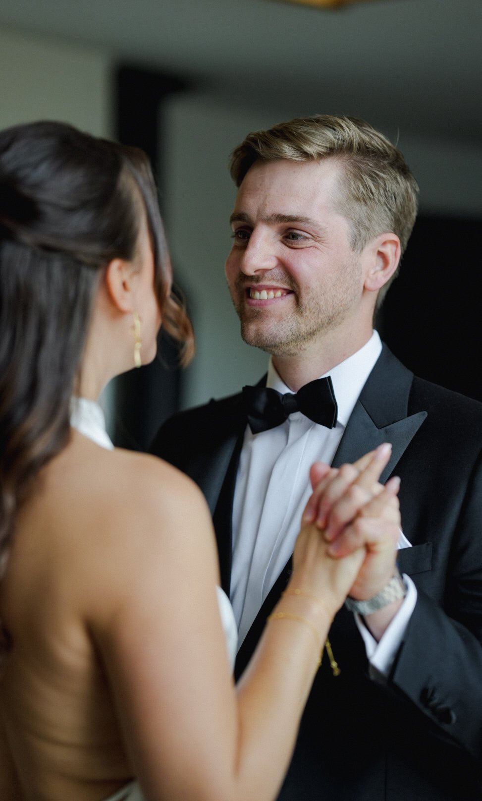 A couple dancing at a formal event, with the man wearing a black tuxedo and the woman in a sleeveless dress.