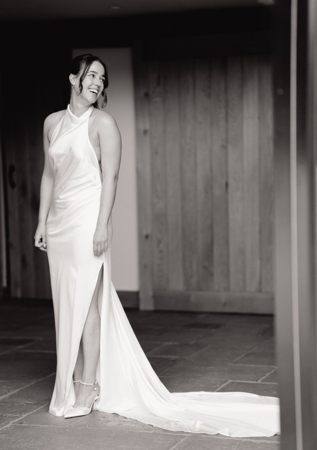 A woman in a white gown standing indoors, smiling and looking to her left.