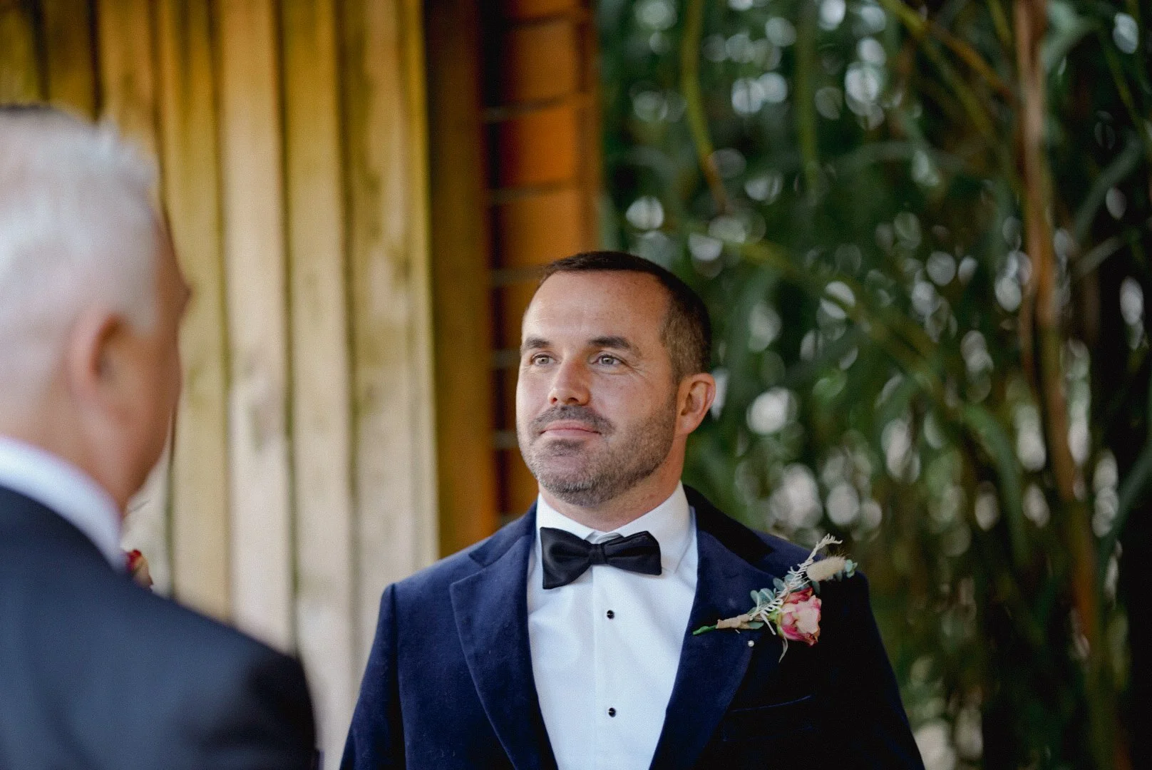 A groom in a tuxedo with a boutonniere, looking at his partner during a wedding ceremony