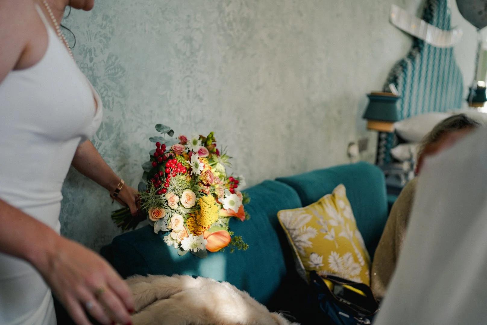 A woman holding a colorful bouquet of flowers, with a teal couch and decorative pillows in the background.