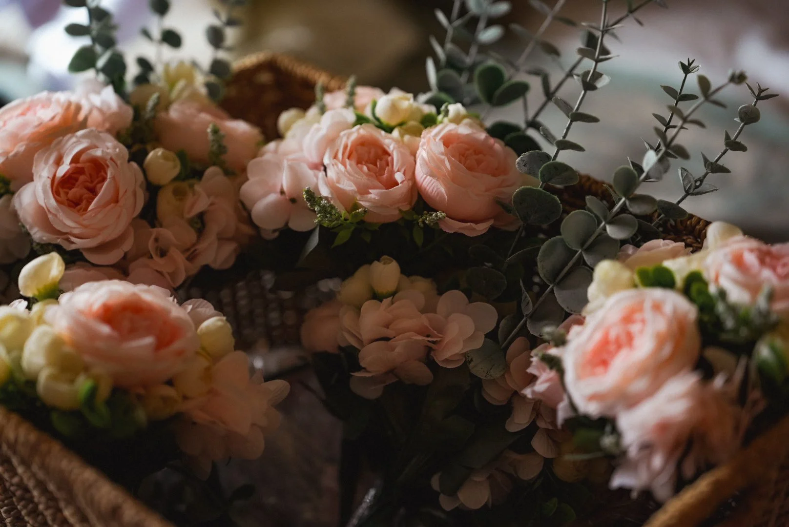 Close-up of pink and cream roses and white hydrangeas in a wicker basket with green foliage.
