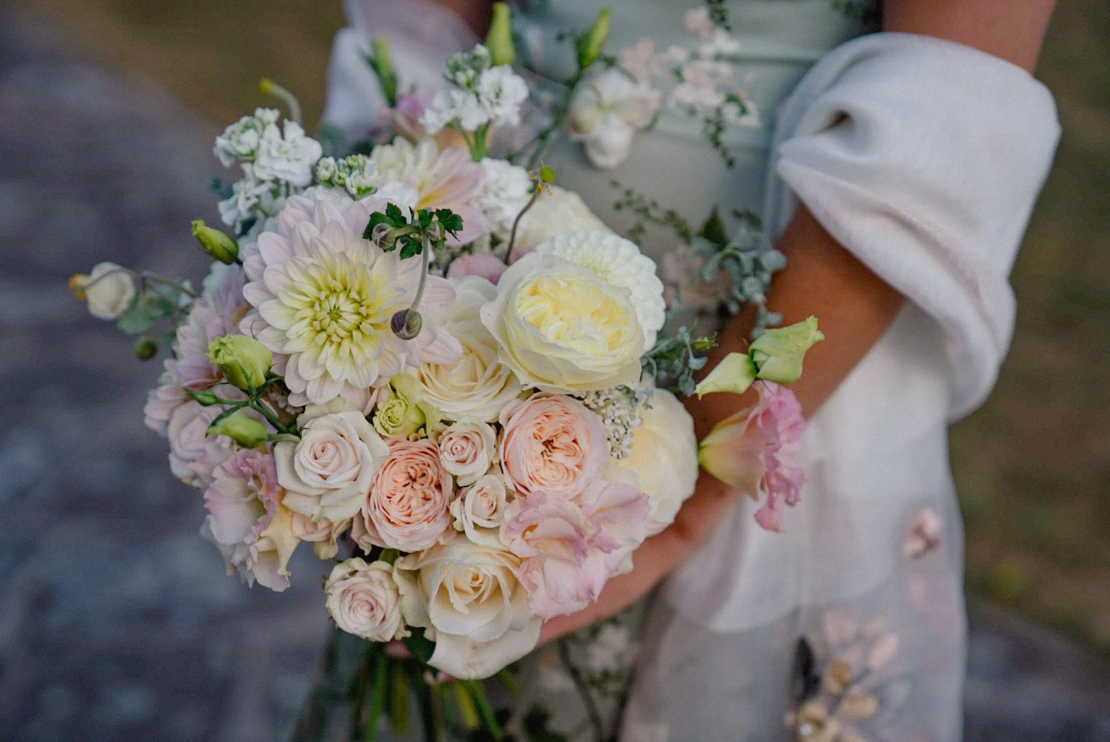 A person holding a bouquet of soft pink, white, and cream-colored flowers with various blooms including roses and peonies.