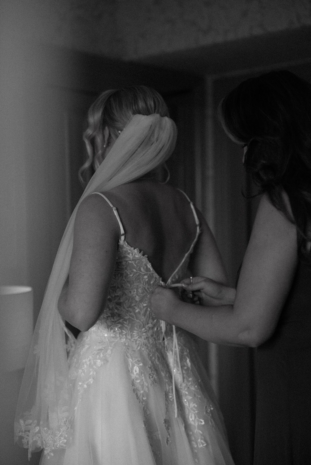 A bride is having her wedding dress fastened by another woman.