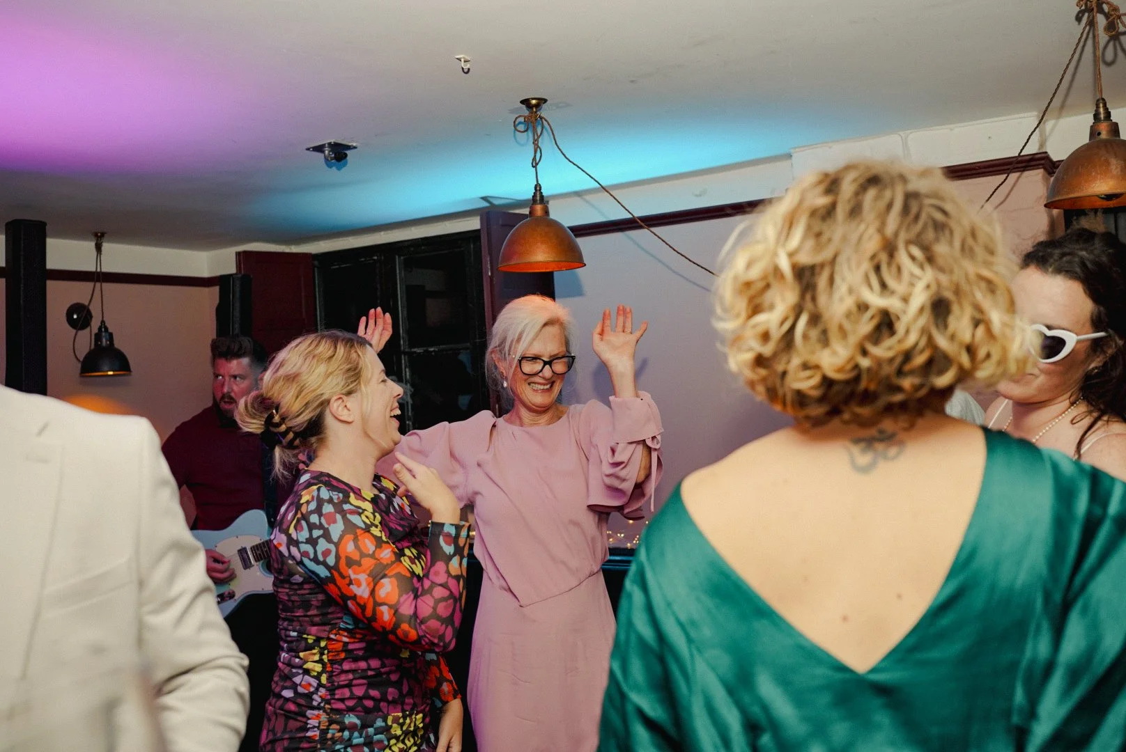 People dancing and celebrating at a party with colorful lighting and hanging lamps.