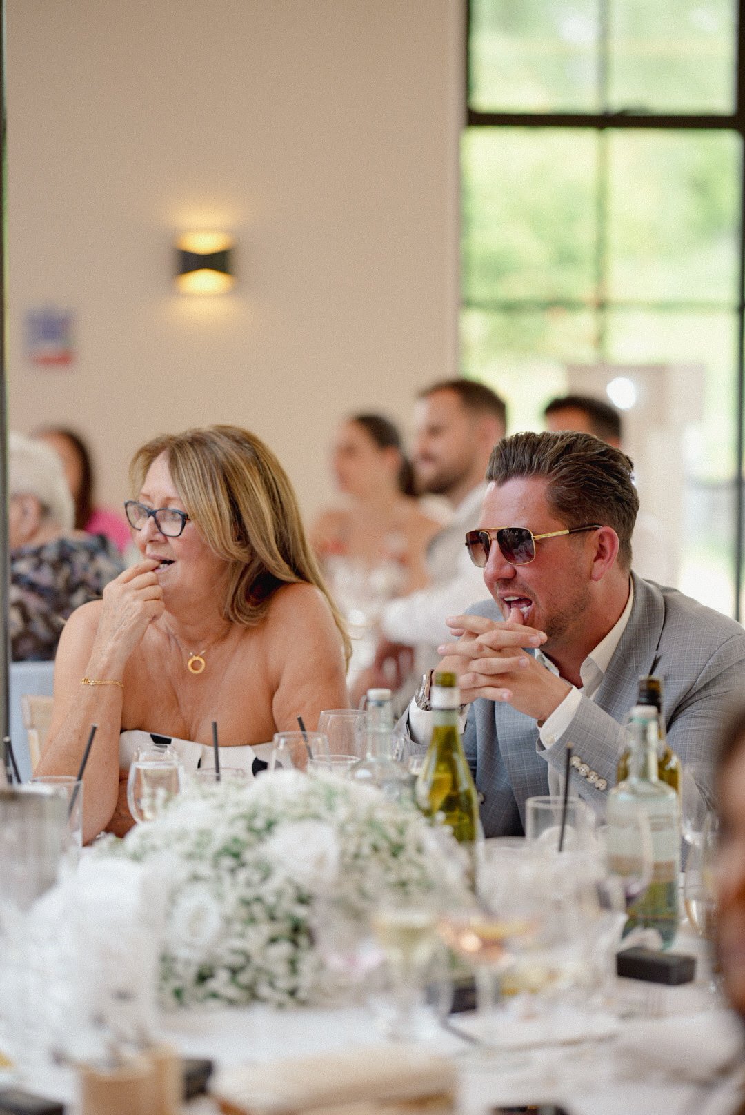 People dressed formally sitting at a table during a celebration, smiling and laughing.
