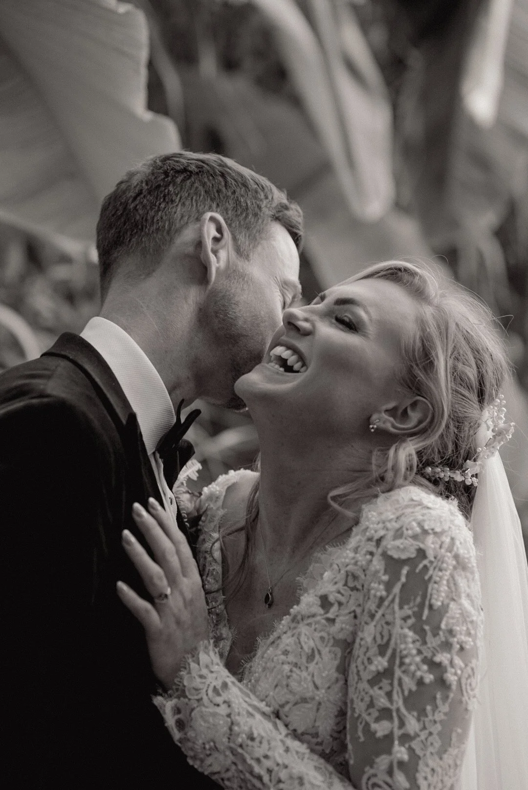 A bride and groom sharing a joyful moment, smiling and laughing, in a close embrace at their wedding.
