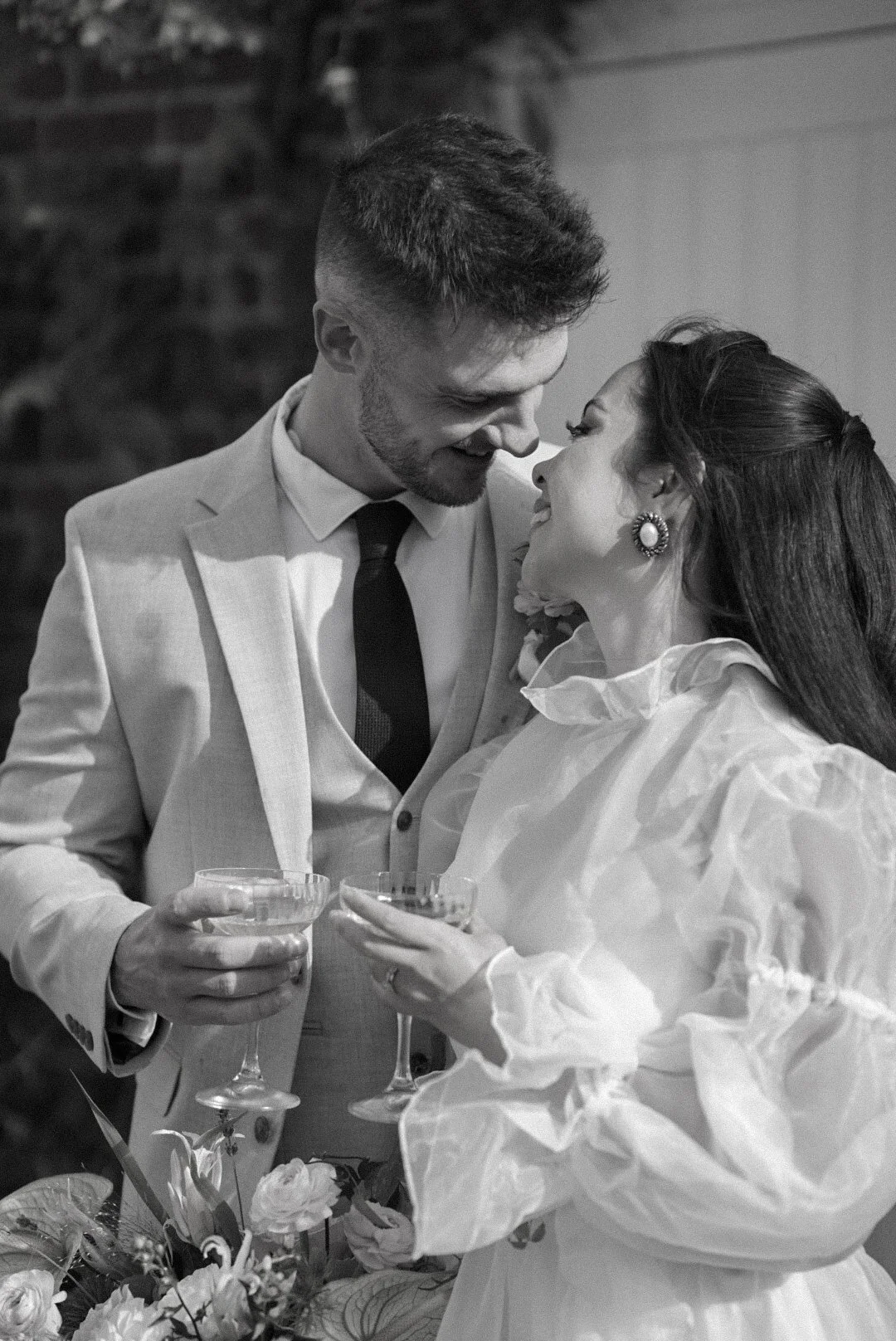 A black and white photo of a joyful couple at a celebration, holding glasses and smiling at each other closely.