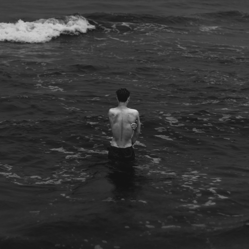 Black-and-white image of a person standing alone in dark ocean water, representing orientation, reflection, and the founder’s effort to read the currents inside the business.