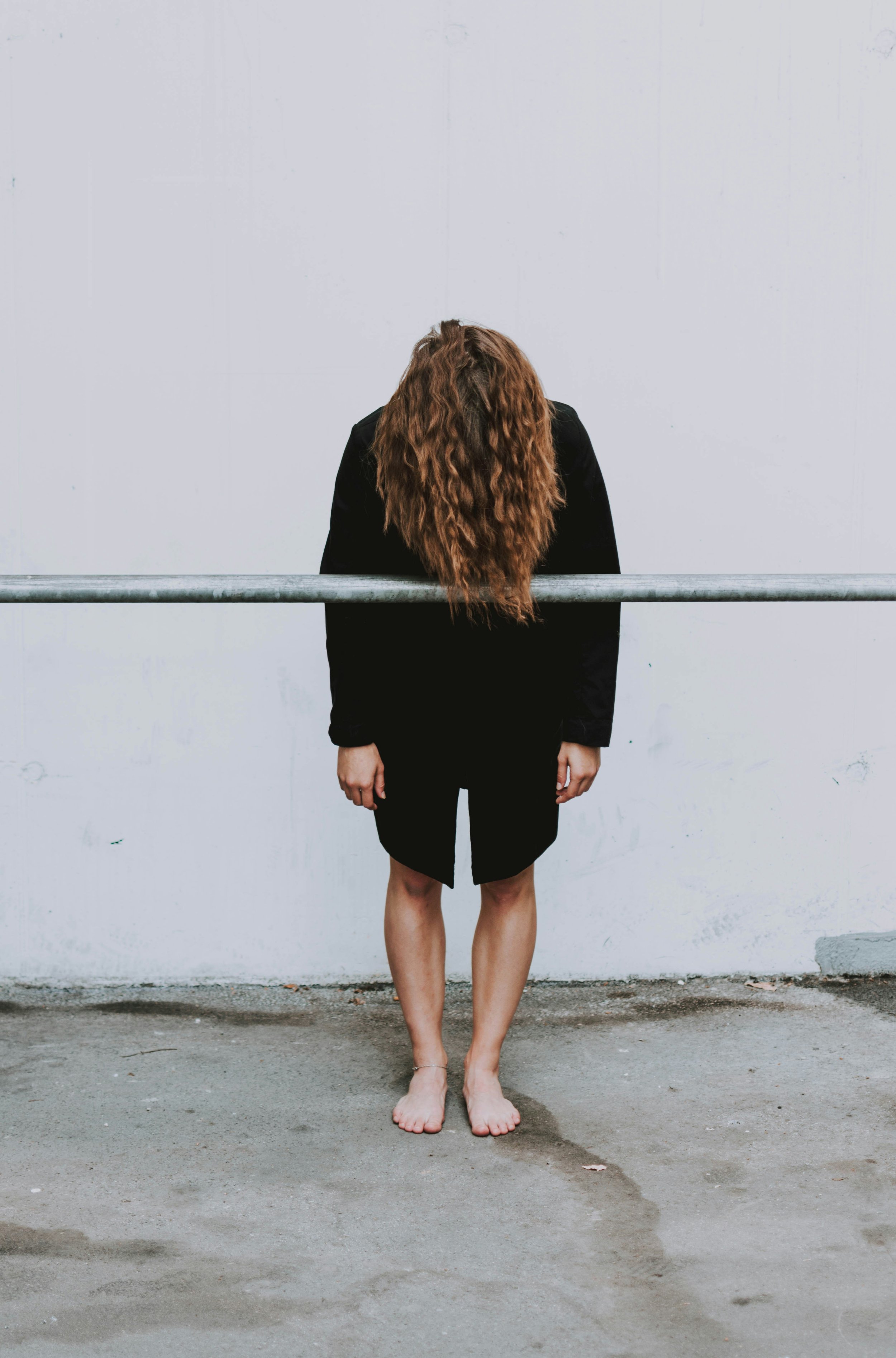 Person standing with head bowed behind a metal railing, representing avoidance, accountability, and the cost of refusing to admit a mistake.