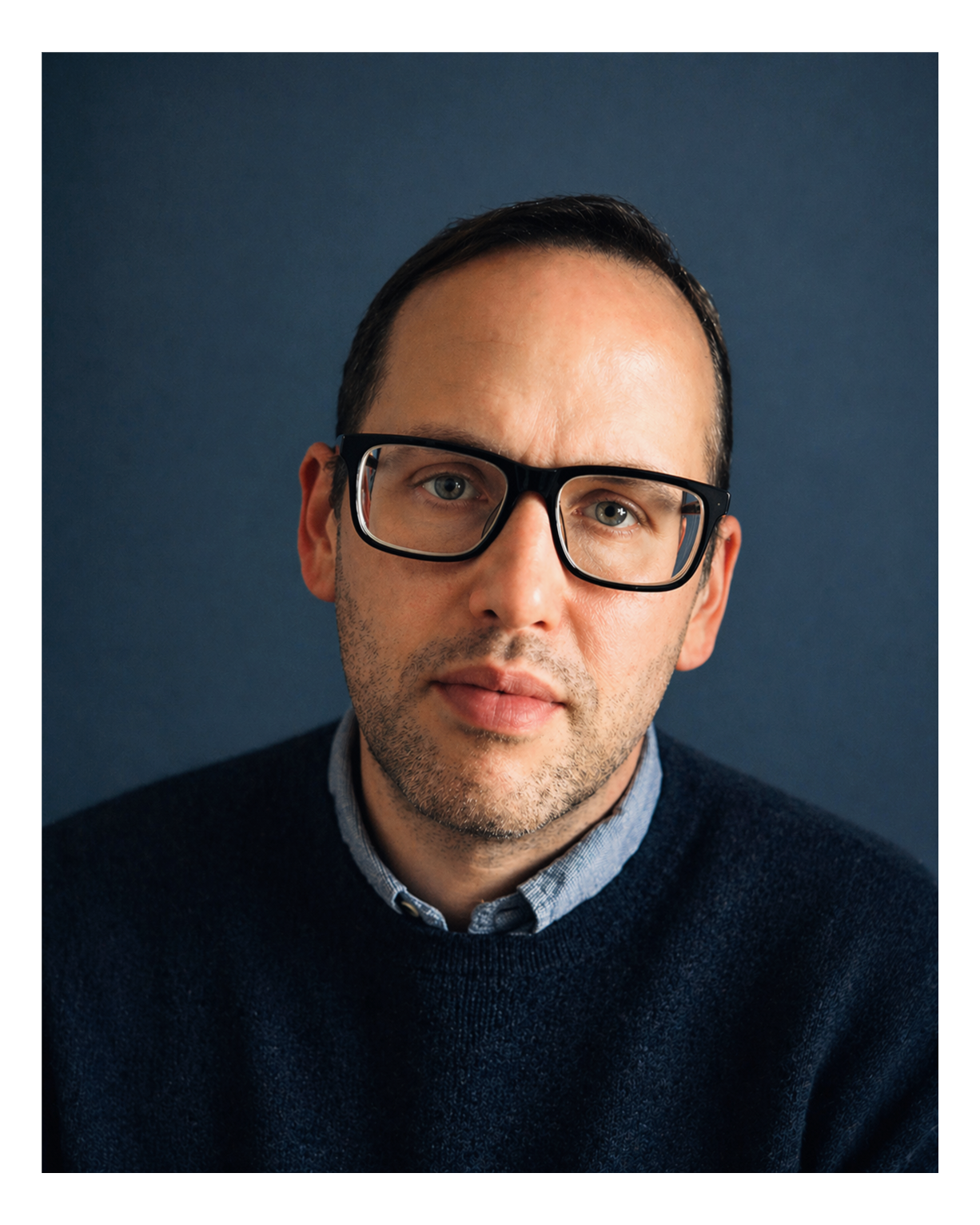 Portrait of Jacob Fisher, founder of NorthBreak Advisors, wearing glasses against a blue studio background.