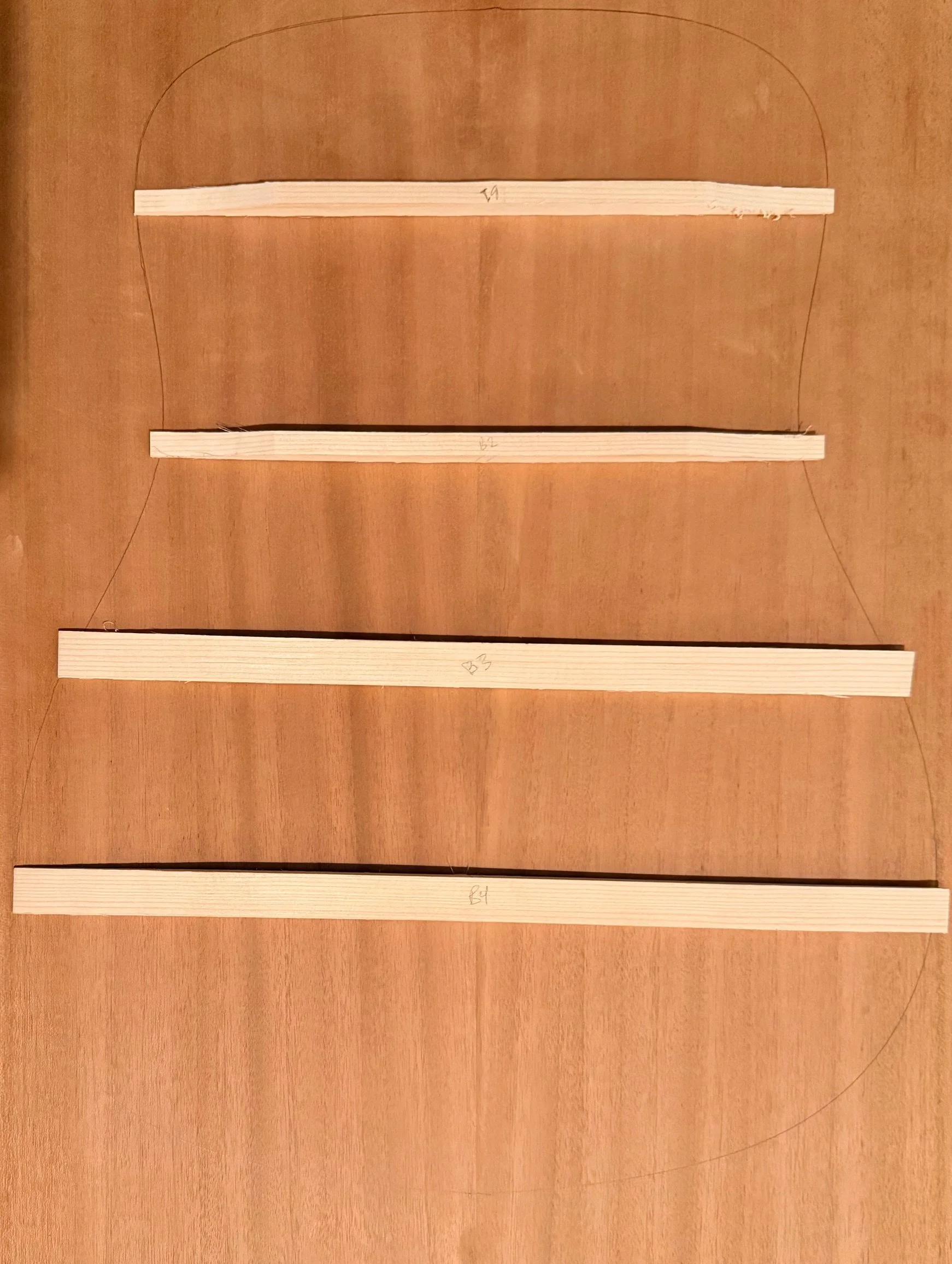 Four wooden slats laid out on a wooden surface, each with handwritten markings and connected by thin wires along the edges.