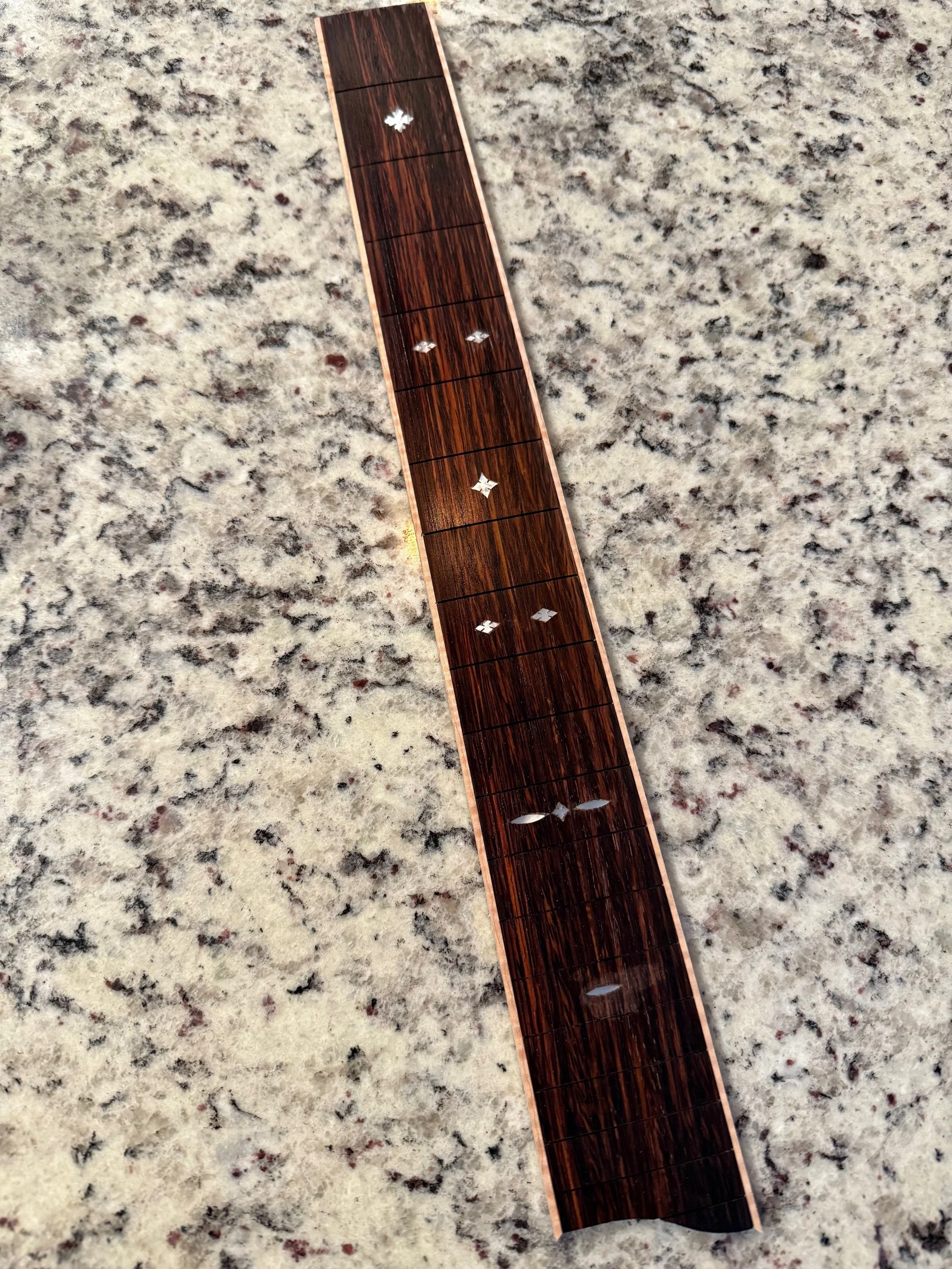 Close-up of a thin, rectangular, wooden inlay strip with decorative star-shaped inlays, placed on a speckled granite surface.