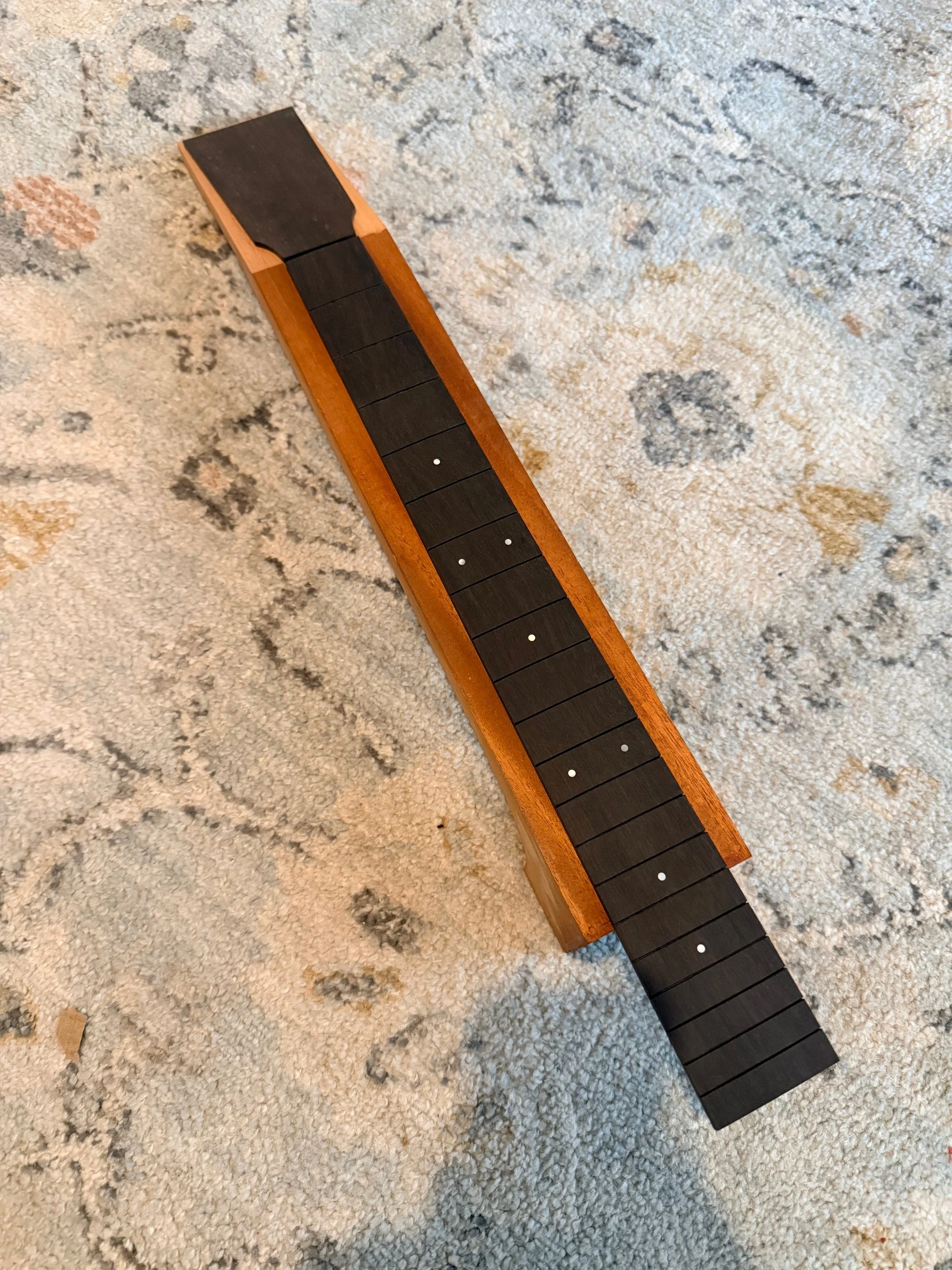 Close-up of a wooden metronome with a black pendulum, placed on a patterned beige carpet.