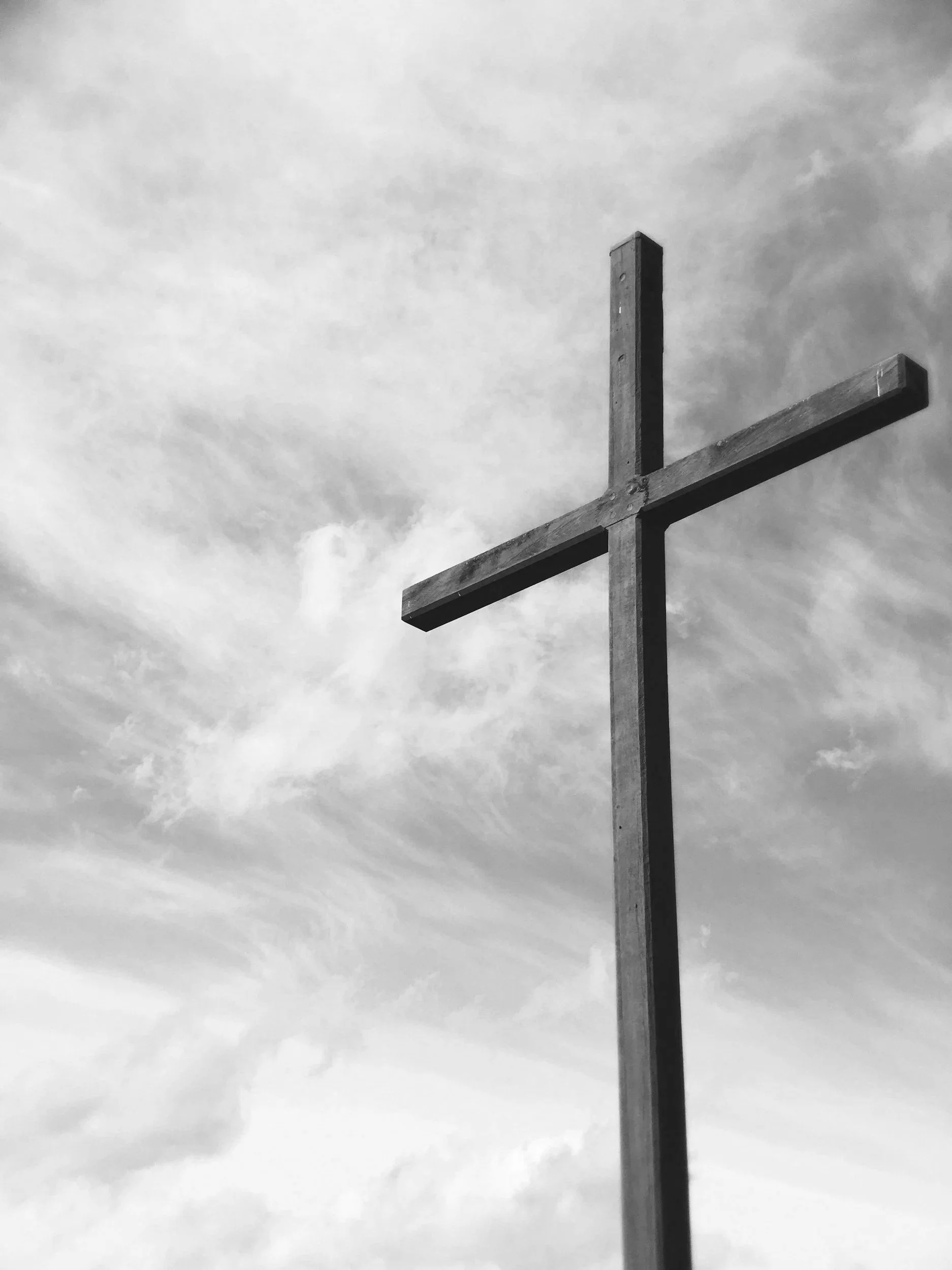 A large wooden cross stands against a cloudy sky, captured in black and white.