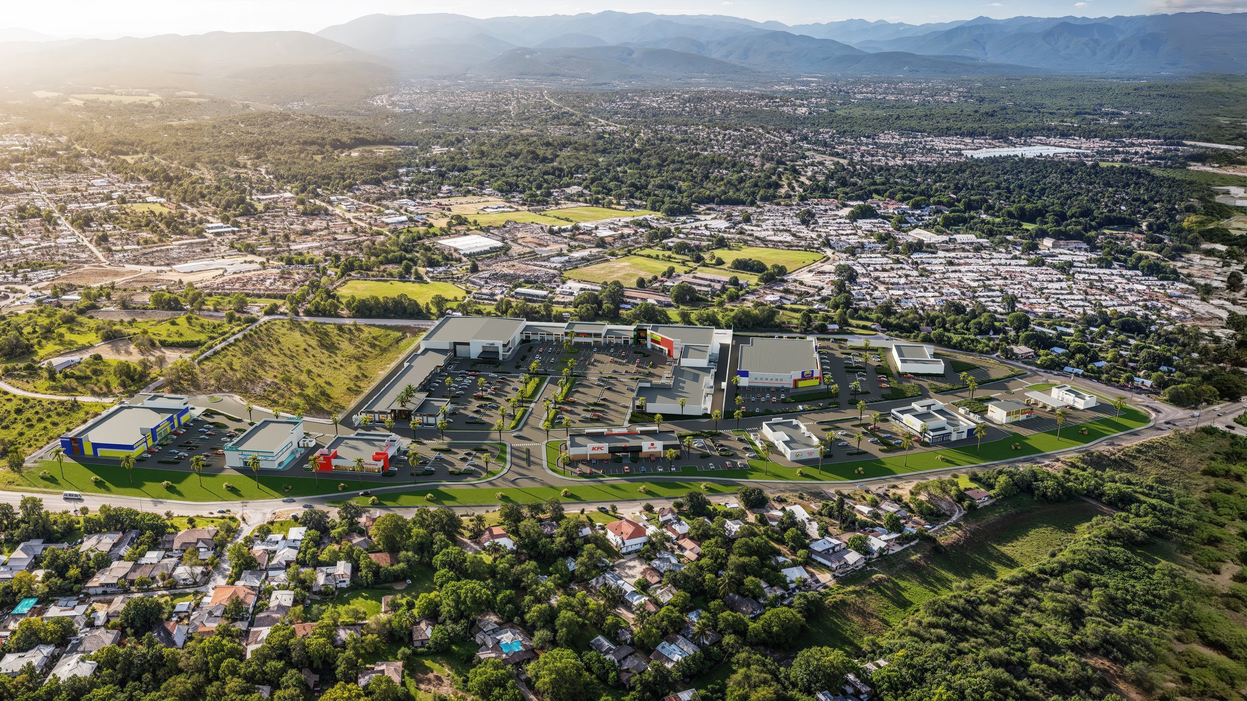 Aerial view of a large shopping complex with multiple stores including KFC, surrounded by parking lots and green space, situated near a residential area and hills.