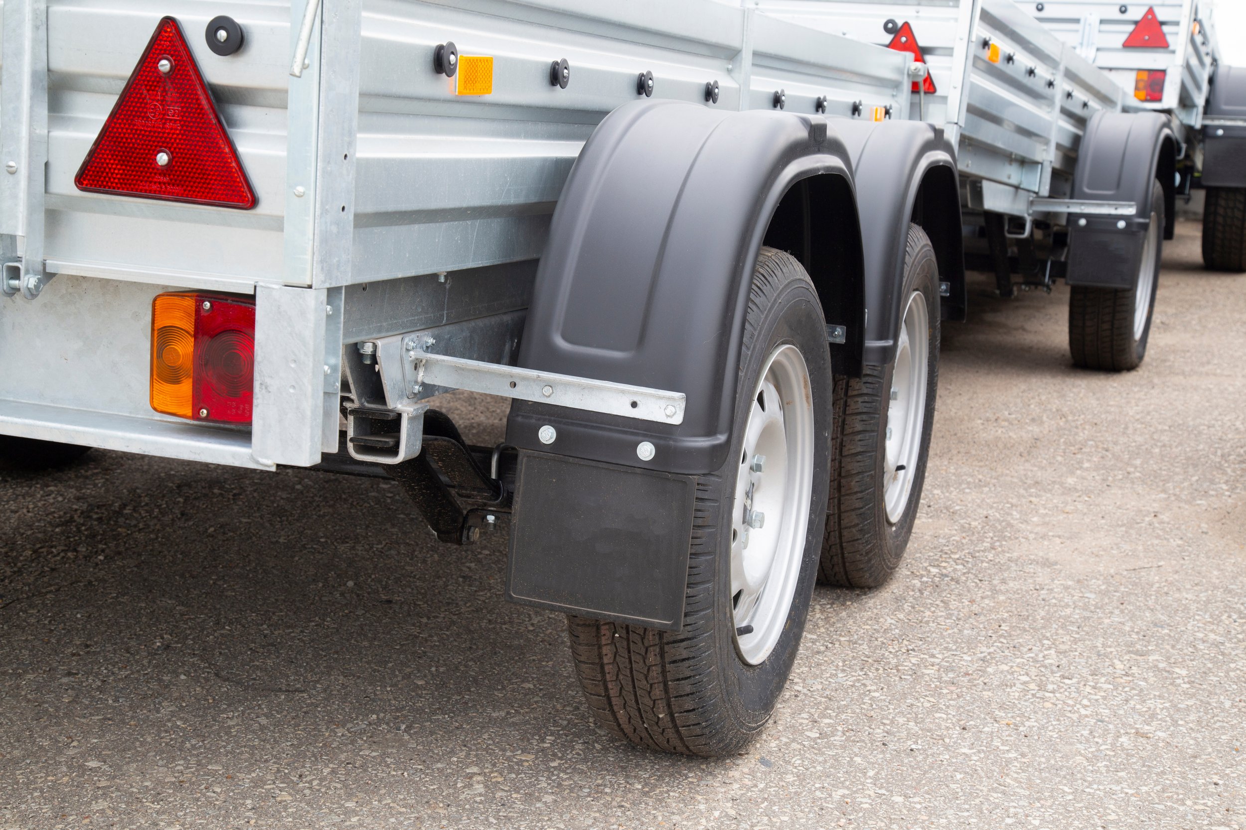 side view of a metal utility trailer with double wheels and rear lights