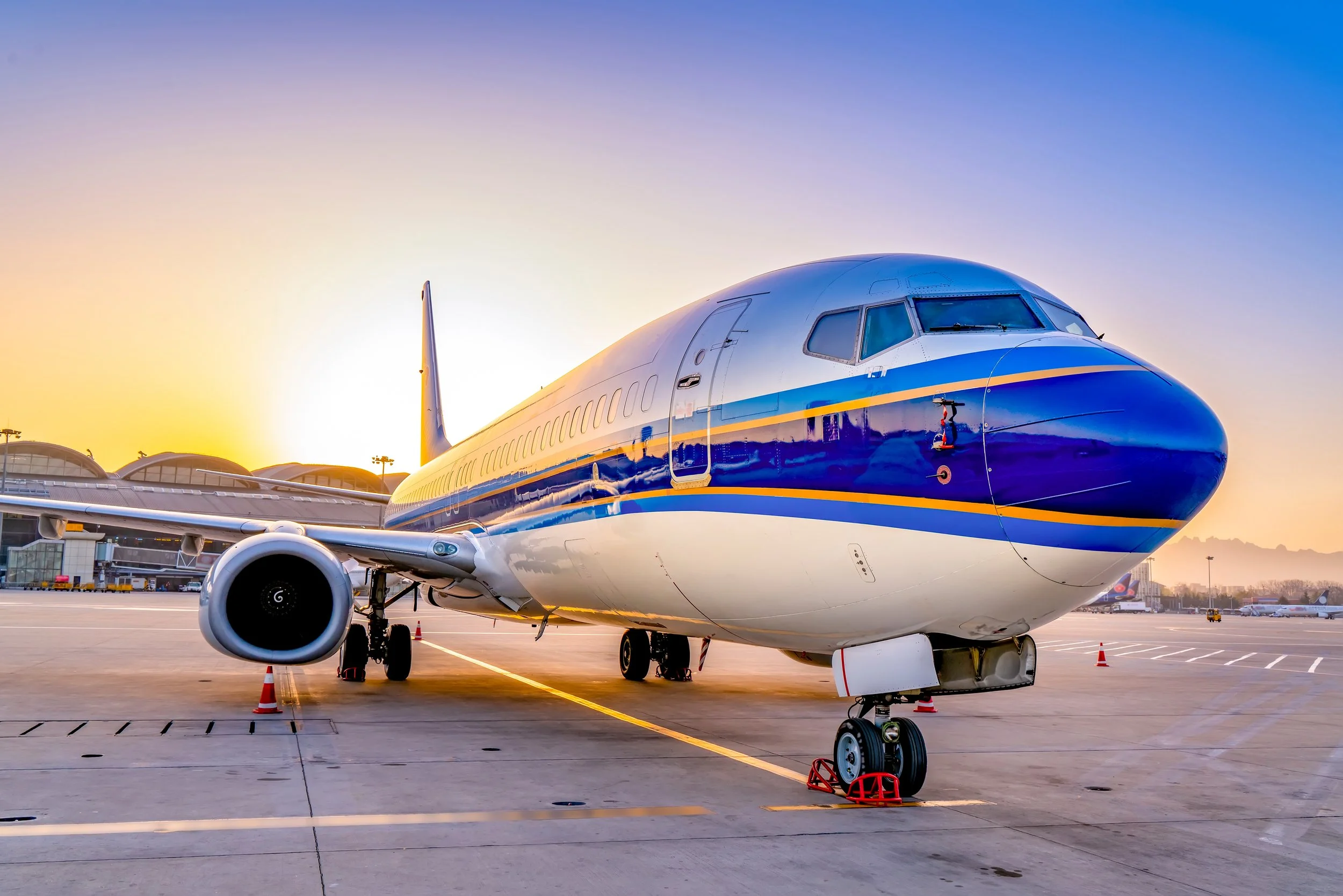 Commercial airplane parked on tarmac at sunset, airport terminal in background.