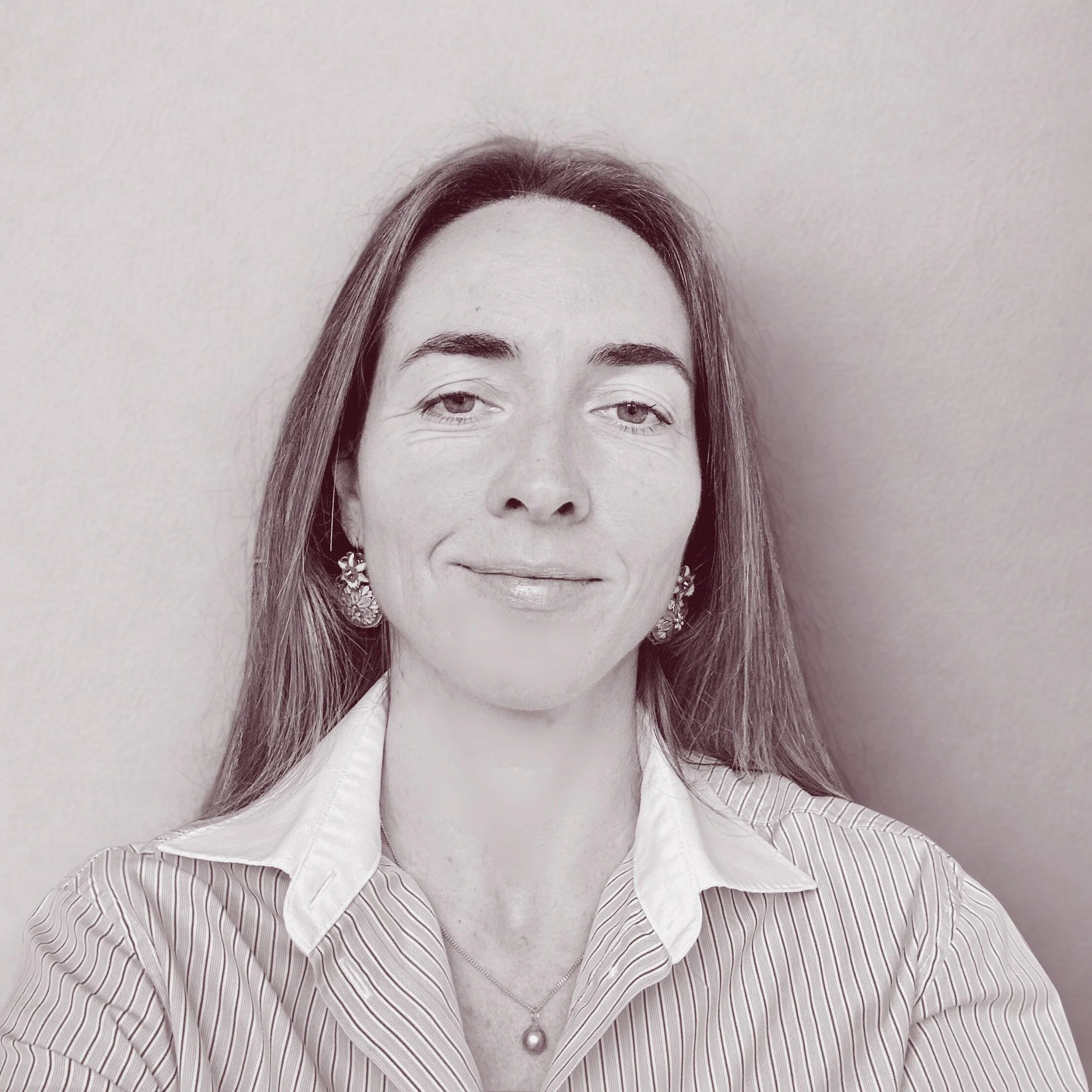 Portrait d'une femme avec des cheveux longs, portant des boucles d'oreilles et un collier, en chemise à col blanc, souriant légèrement, photo en noir et blanc.