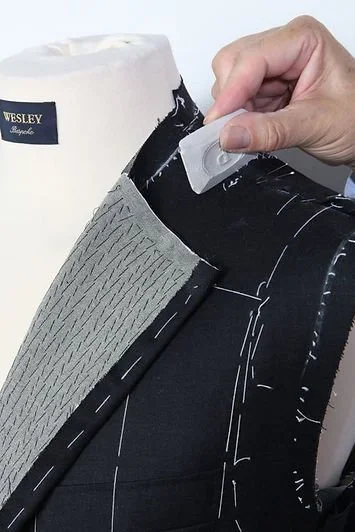 A person using a white tool to sew black fabric with gray textured fabric attached in a sewing or tailoring process.
