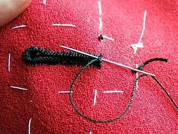 Close-up of a sewing needle, black thread, and white chalk markings on red fabric, indicating fabric sewing or tailoring.
