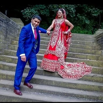 A man in a blue suit and a woman in a red traditional dress posing on outdoor stone steps.